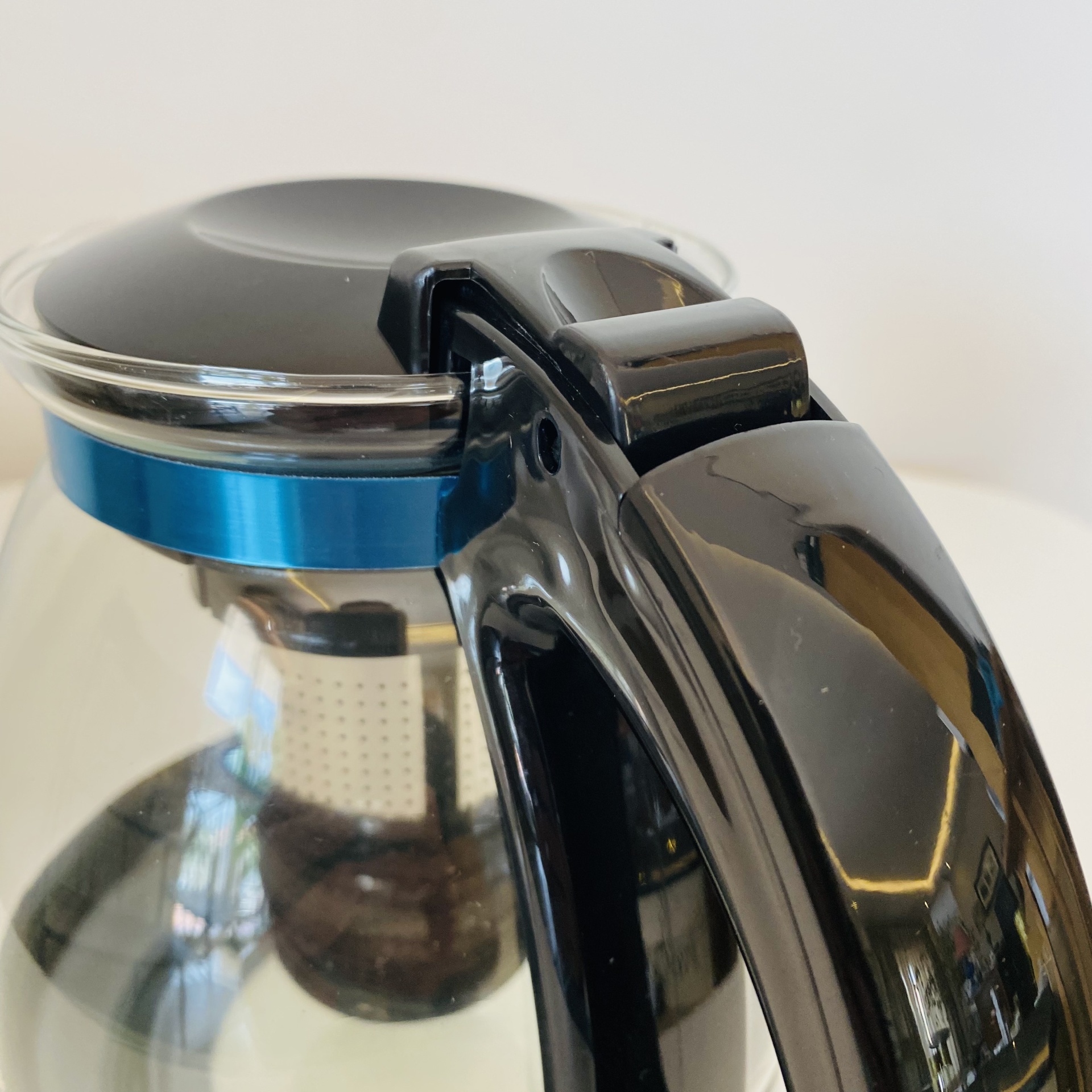 Jarra de chá de vidro com tampa preta e filtro, destaque no punho e detalhe azul.