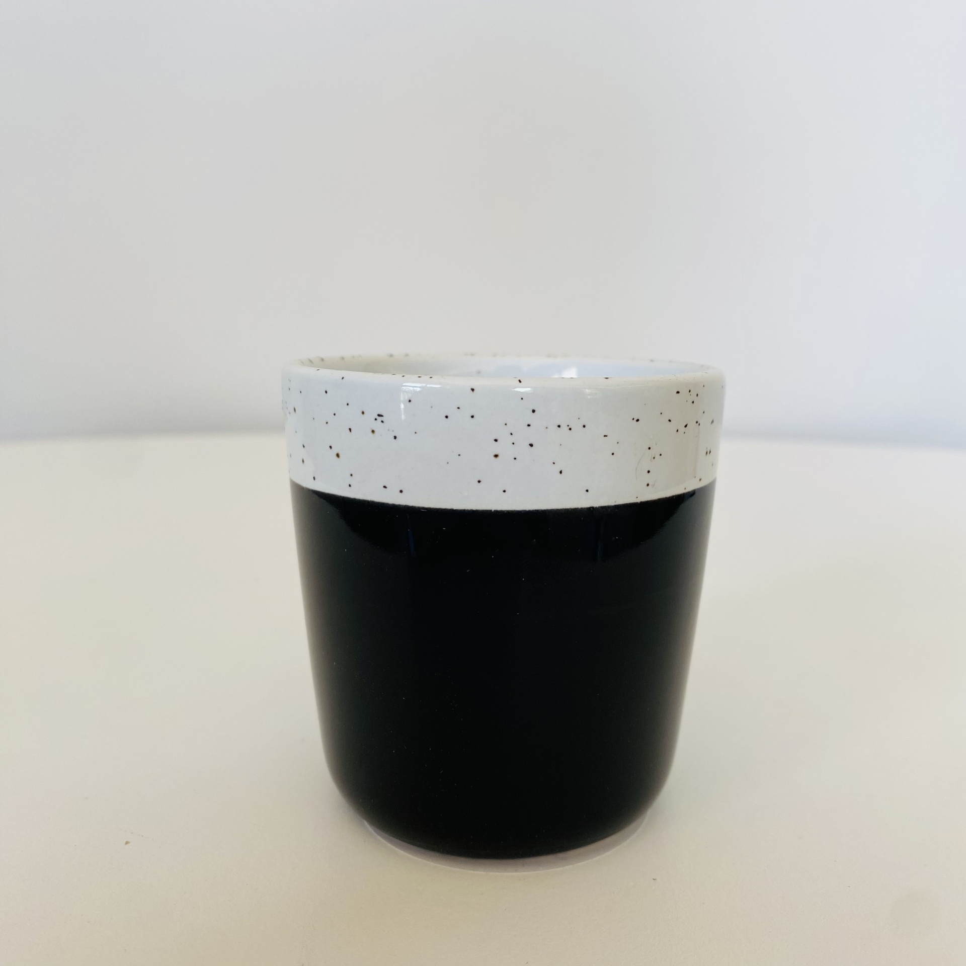 Vaso pequeno cerâmico preto e branco com manchas negras na parte superior.