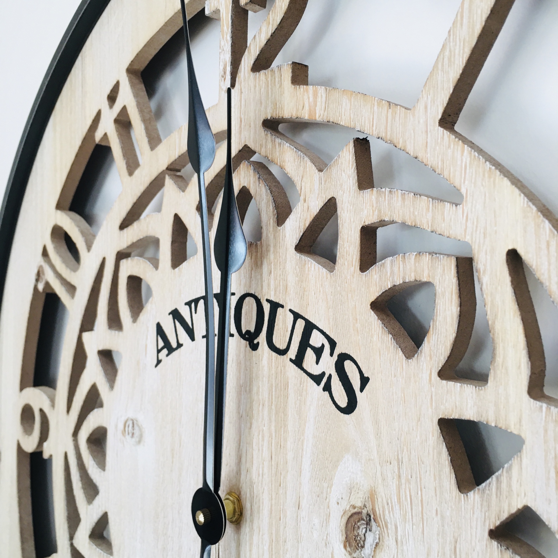 Relógio de parede de madeira clara com números romanos recortados e ponteiros pretos