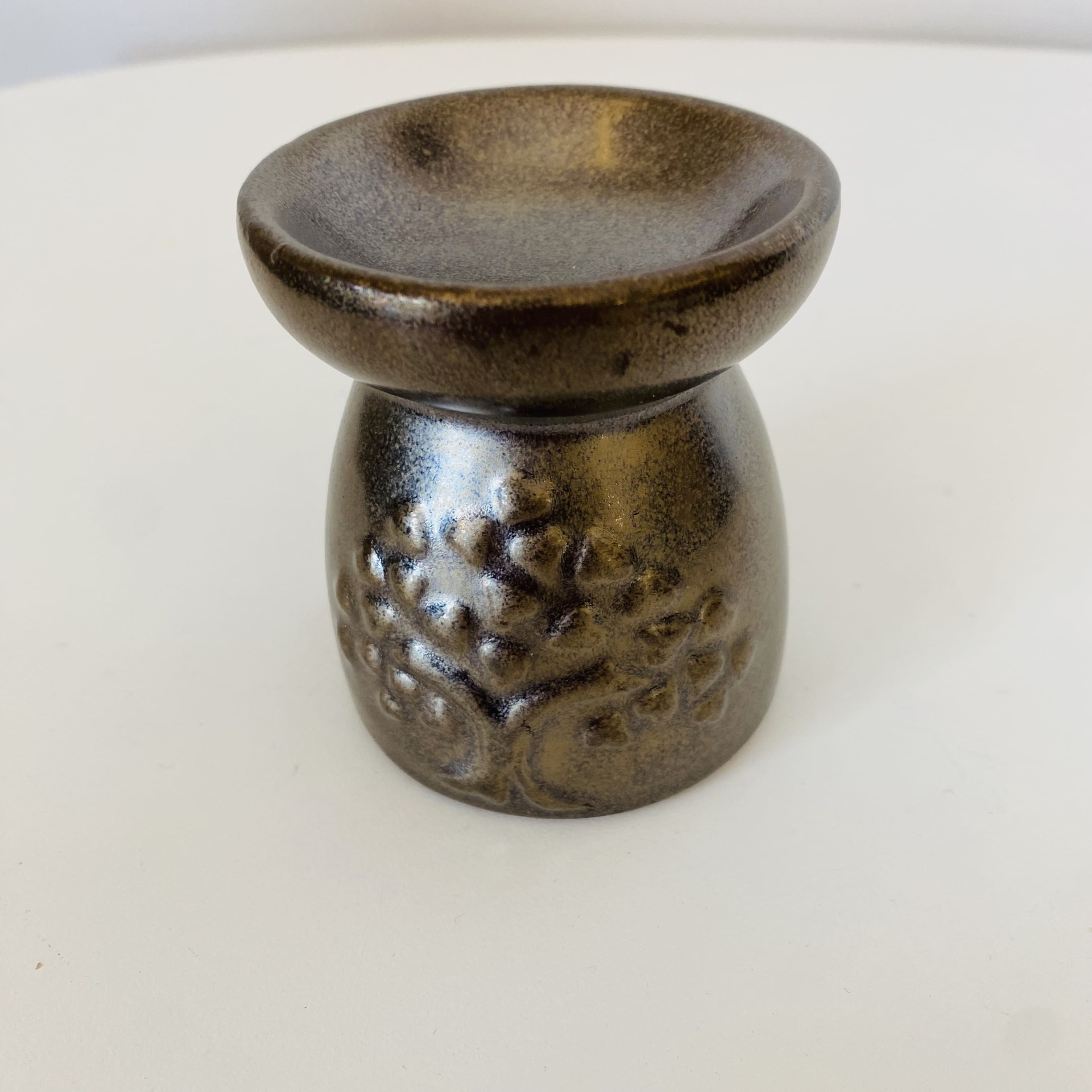 Pequeno objeto de cerâmica castanha com relevos de árvore e superfície brilhante