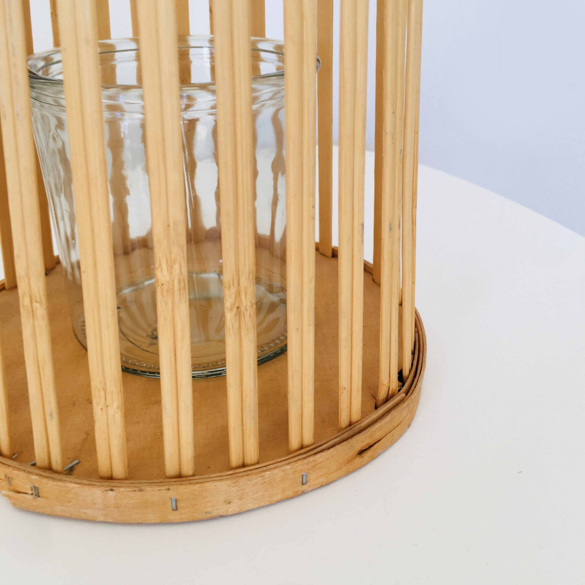 Castiçal de vidro com estrutura de vime sobre mesa branca