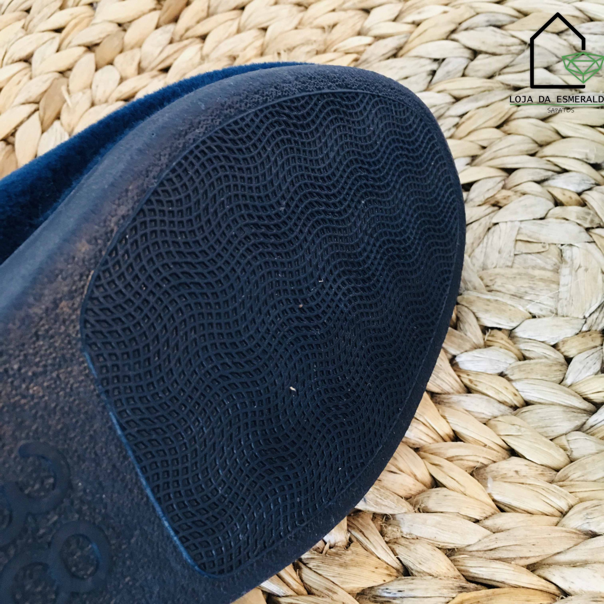 Sola de calçado azul escuro com padrão texturizado sobre tapete de fibras naturais