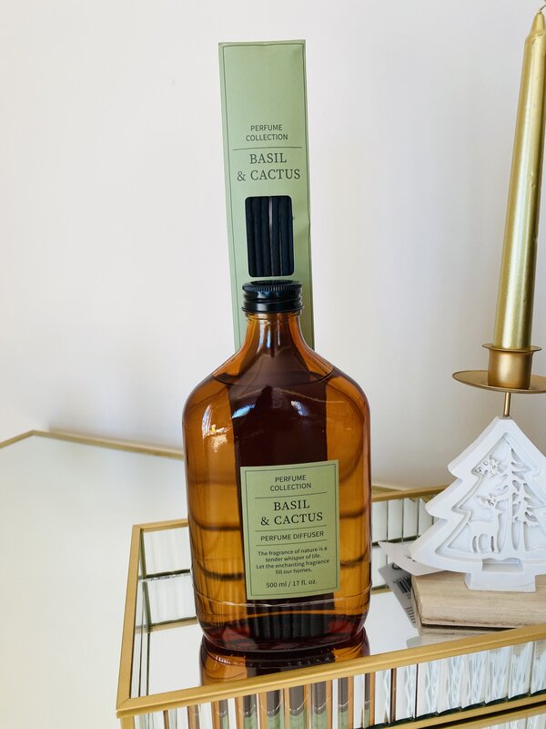 Difusor de perfume âmbar Basil & Cactus com sticks pretos num tabuleiro dourado com espelho e decoração de Natal branca e vela dourada