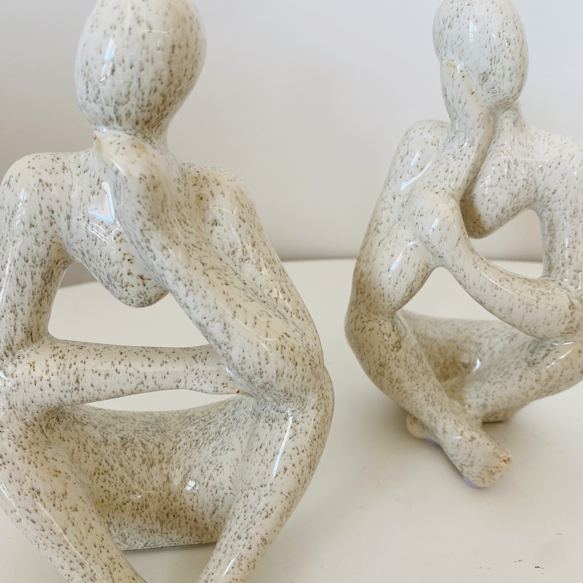Esculturas abstratas de figuras humanas em cerâmica branca com detalhes cinza, sentadas