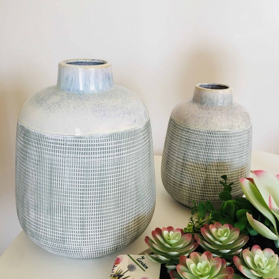 Dois vasos cerâmicos cinza com padrão de linhas brancas e suculentas artificiais ao lado.