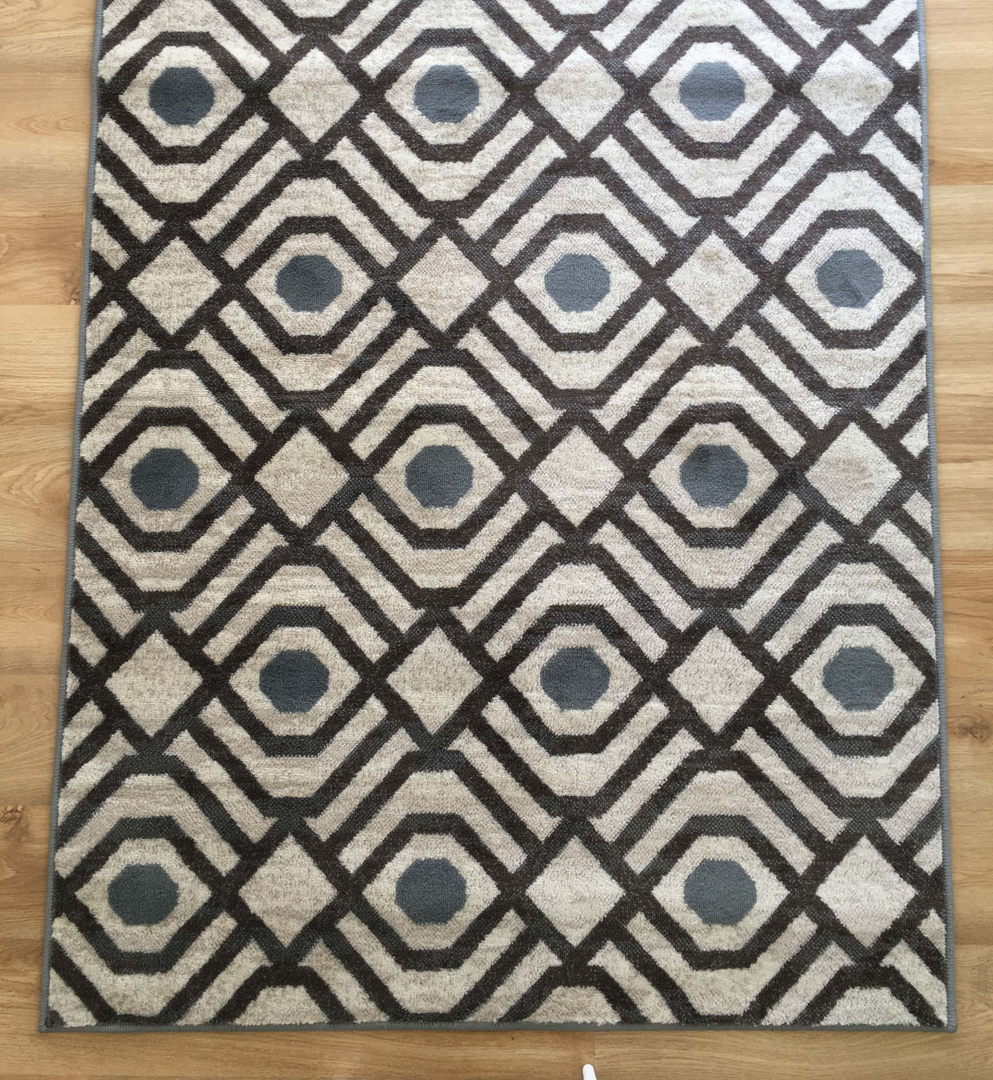 Tapete geométrico cinzento, preto e bege sobre chão de madeira clara