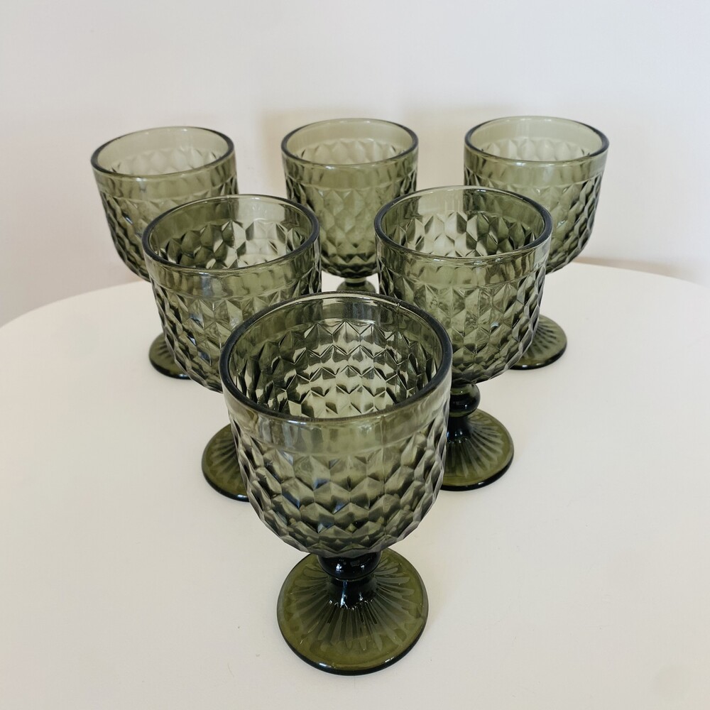 Seis copos verdes escuros com padrão facetado em mesa branca