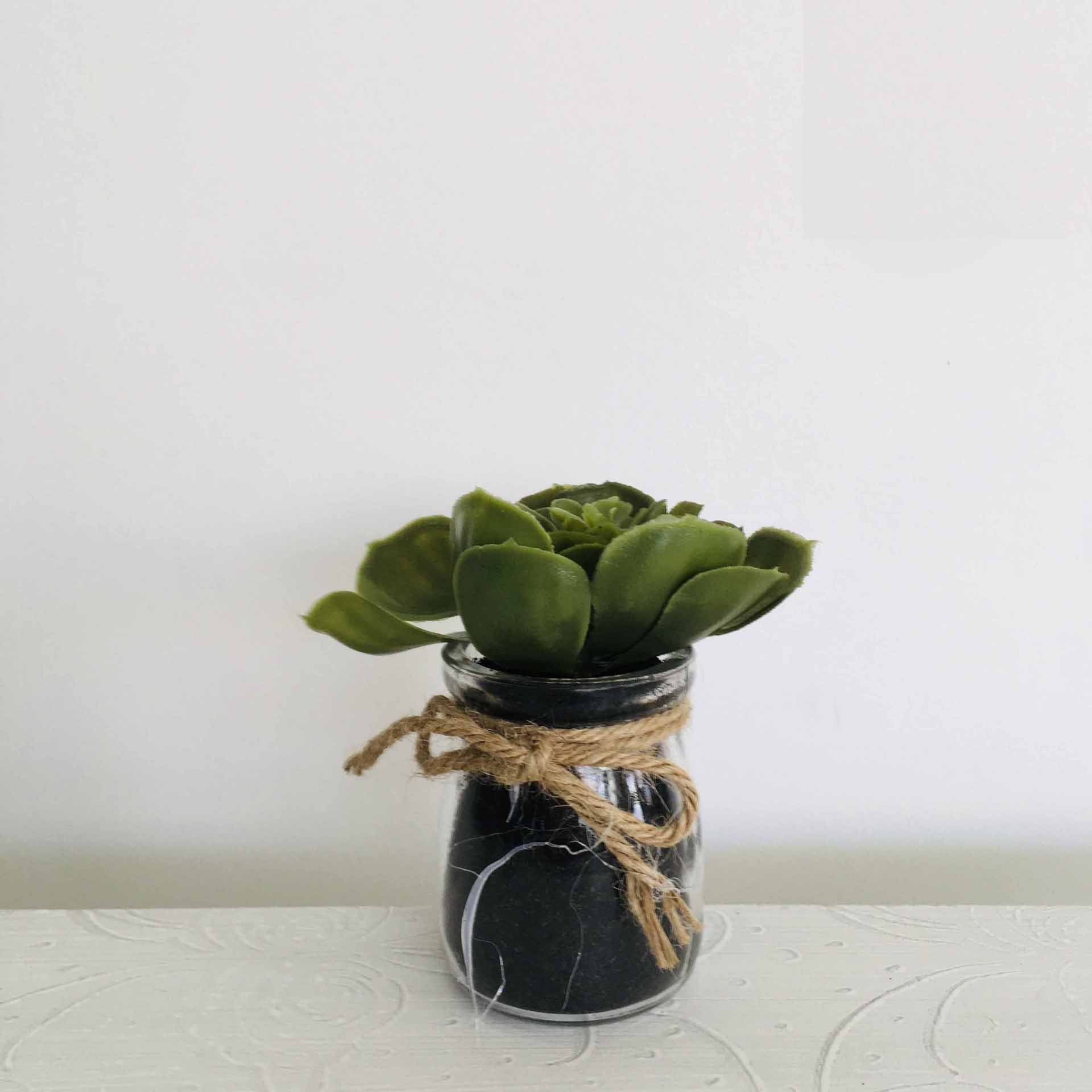Jarro pequeno de vidro preto com cordão de ráfia e planta verde artificial