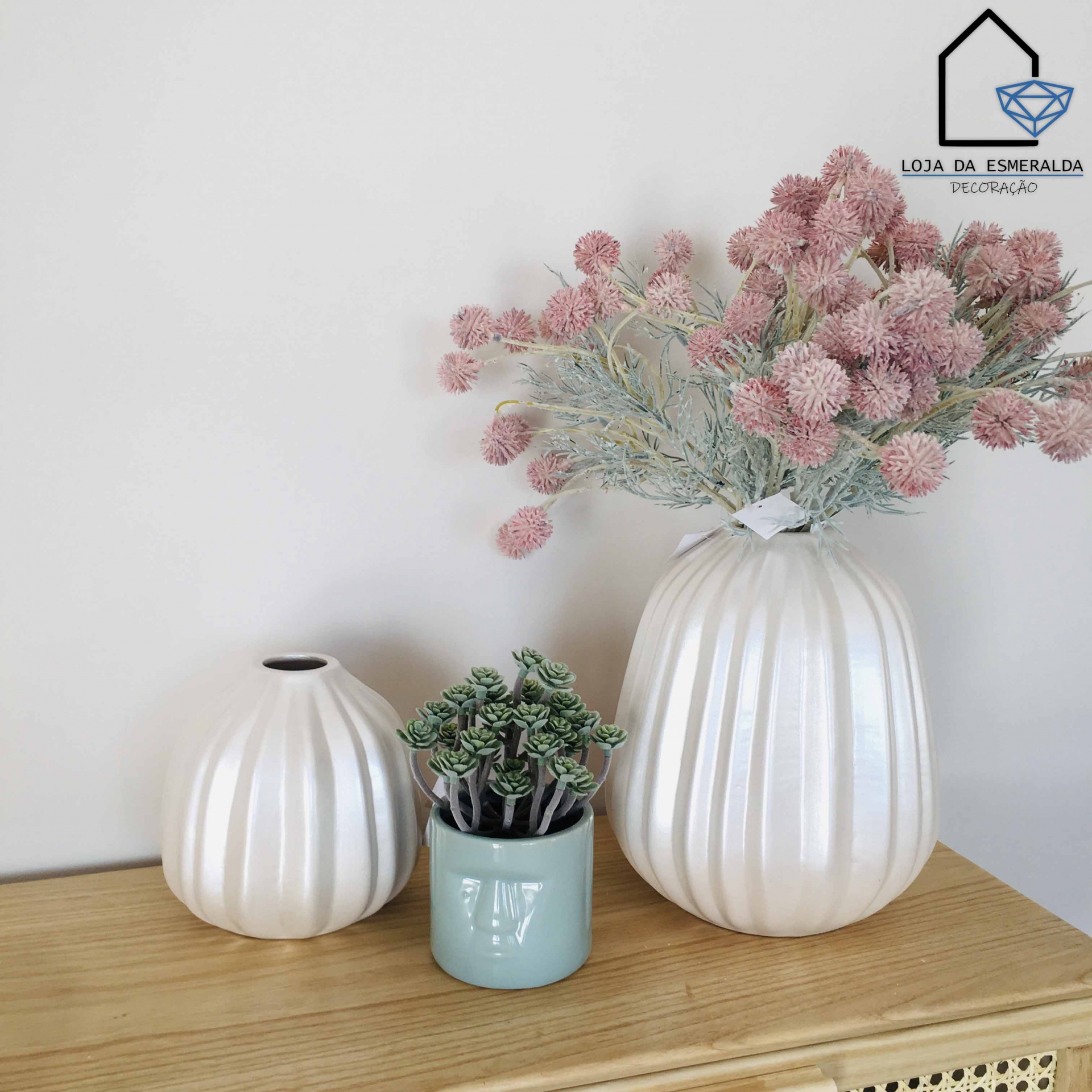 Três vasos decorativos em cerâmica branca com plantas artificiais sobre madeira clara