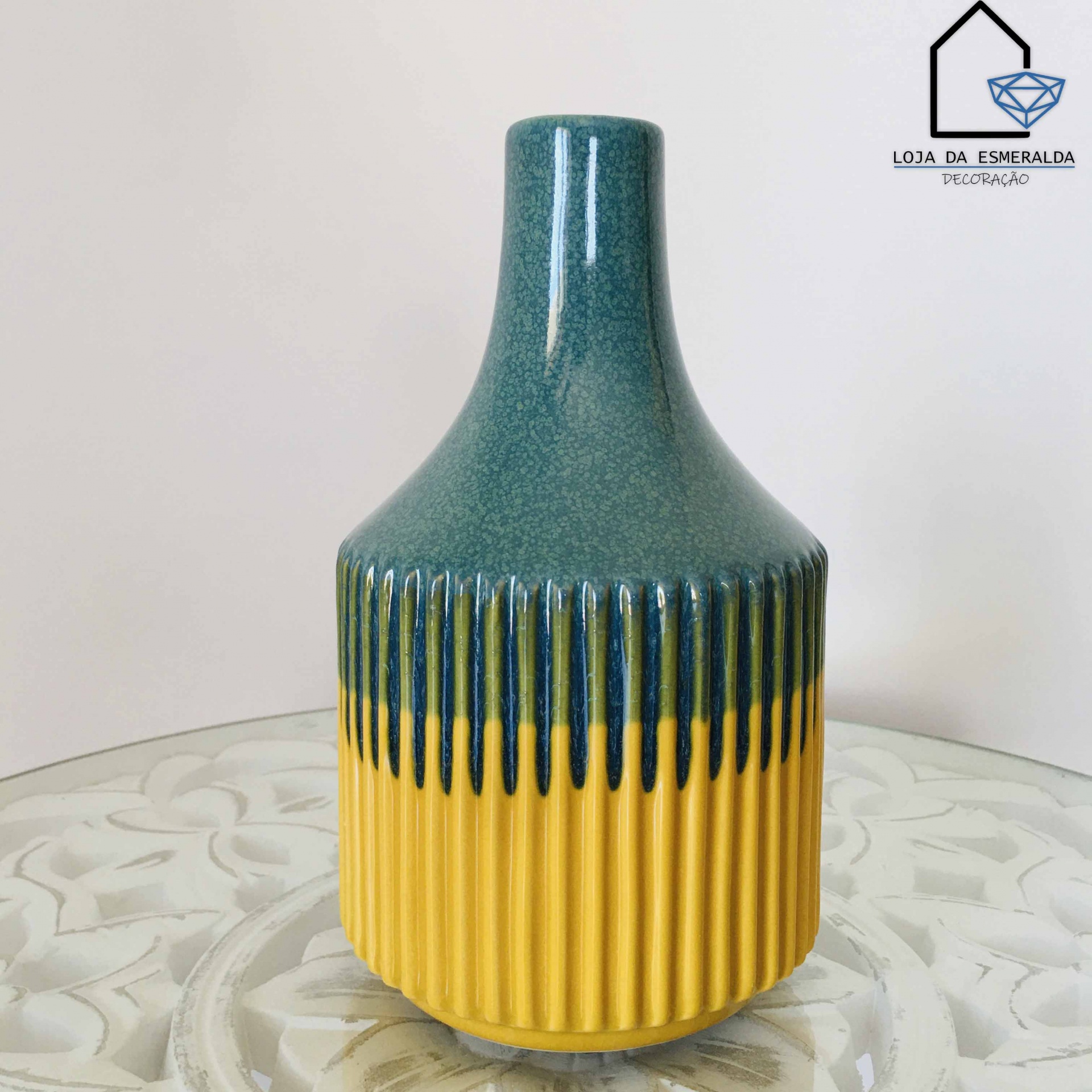 Vaso decorativo cerâmico verde azulado e amarelo com relevo vertical sobre mesa de vidro