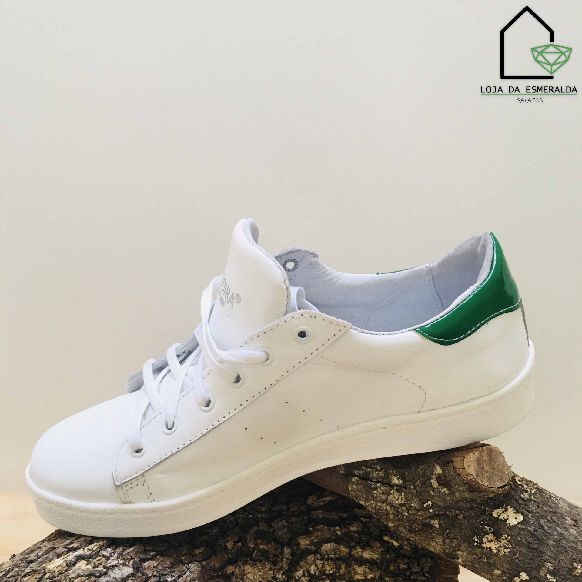 Tênis branco com detalhe verde no calcanhar sobre tronco de árvore
