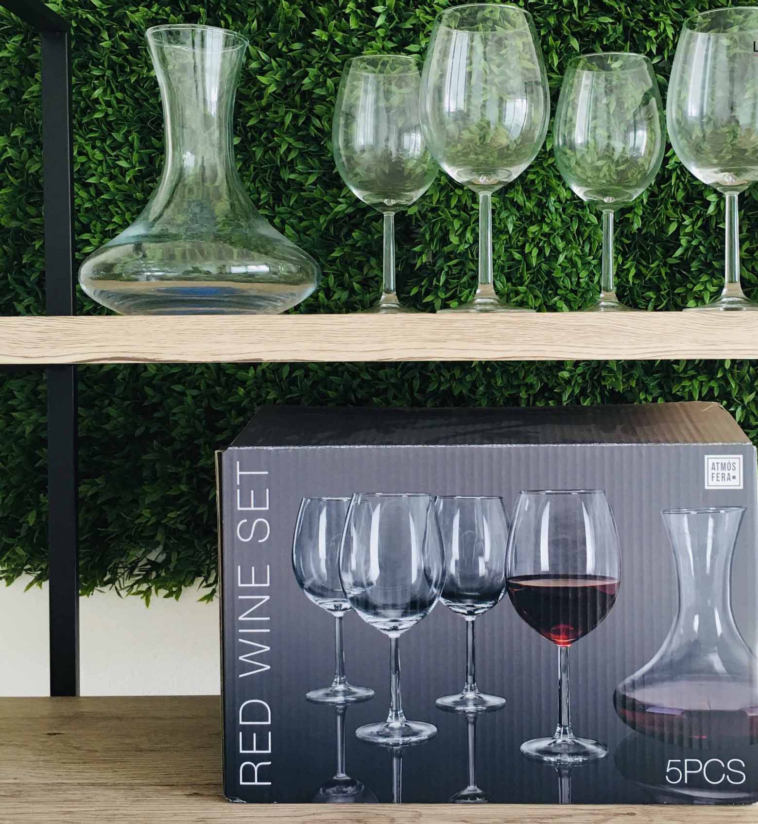 Conjunto de garrafa decantadora e copos de vinho em vidro transparente sobre prateleira de madeira com caixa preta na prateleira inferior