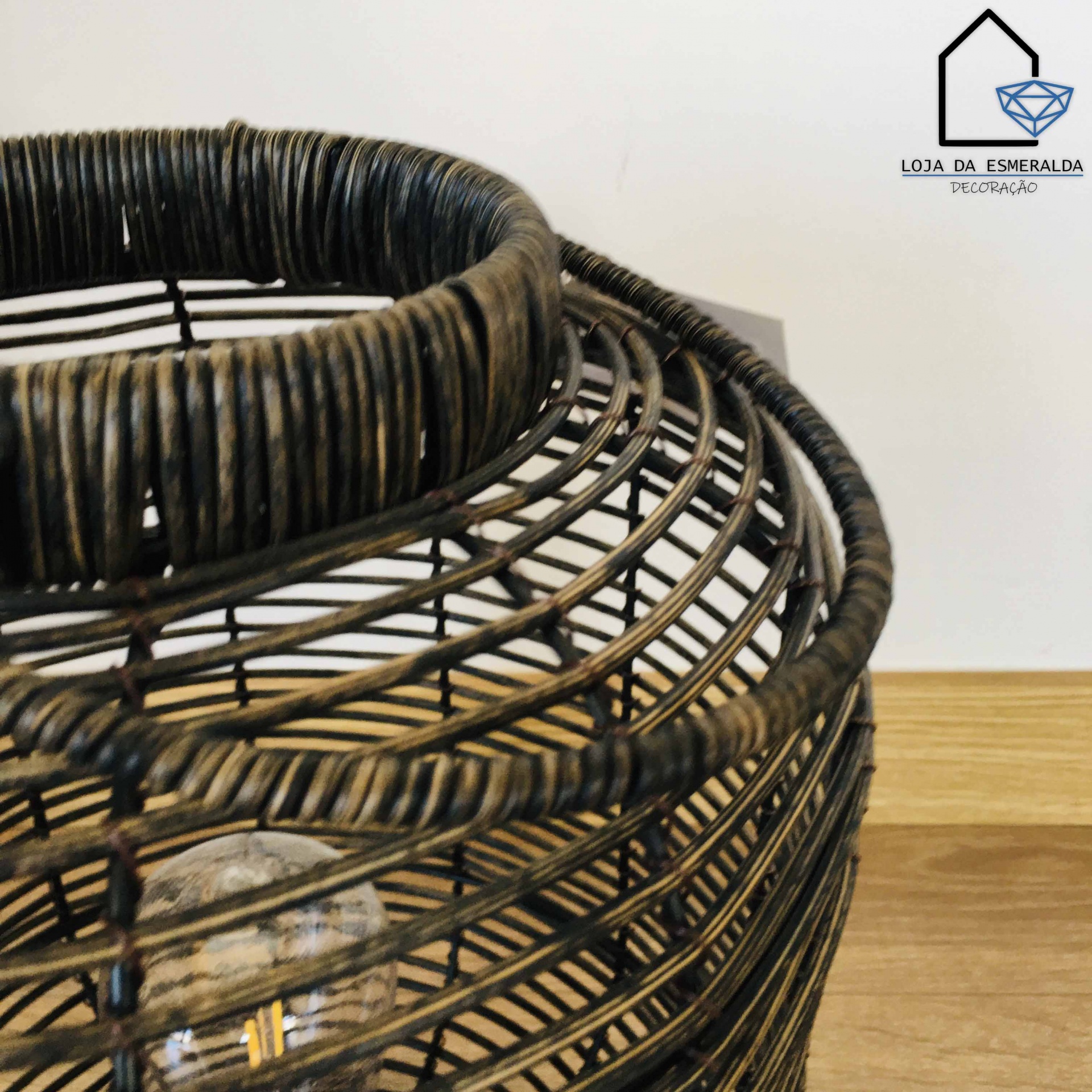 Luminária de teto redonda em rattan preto entrelaçado com lâmpada visível e chão de madeira clara.