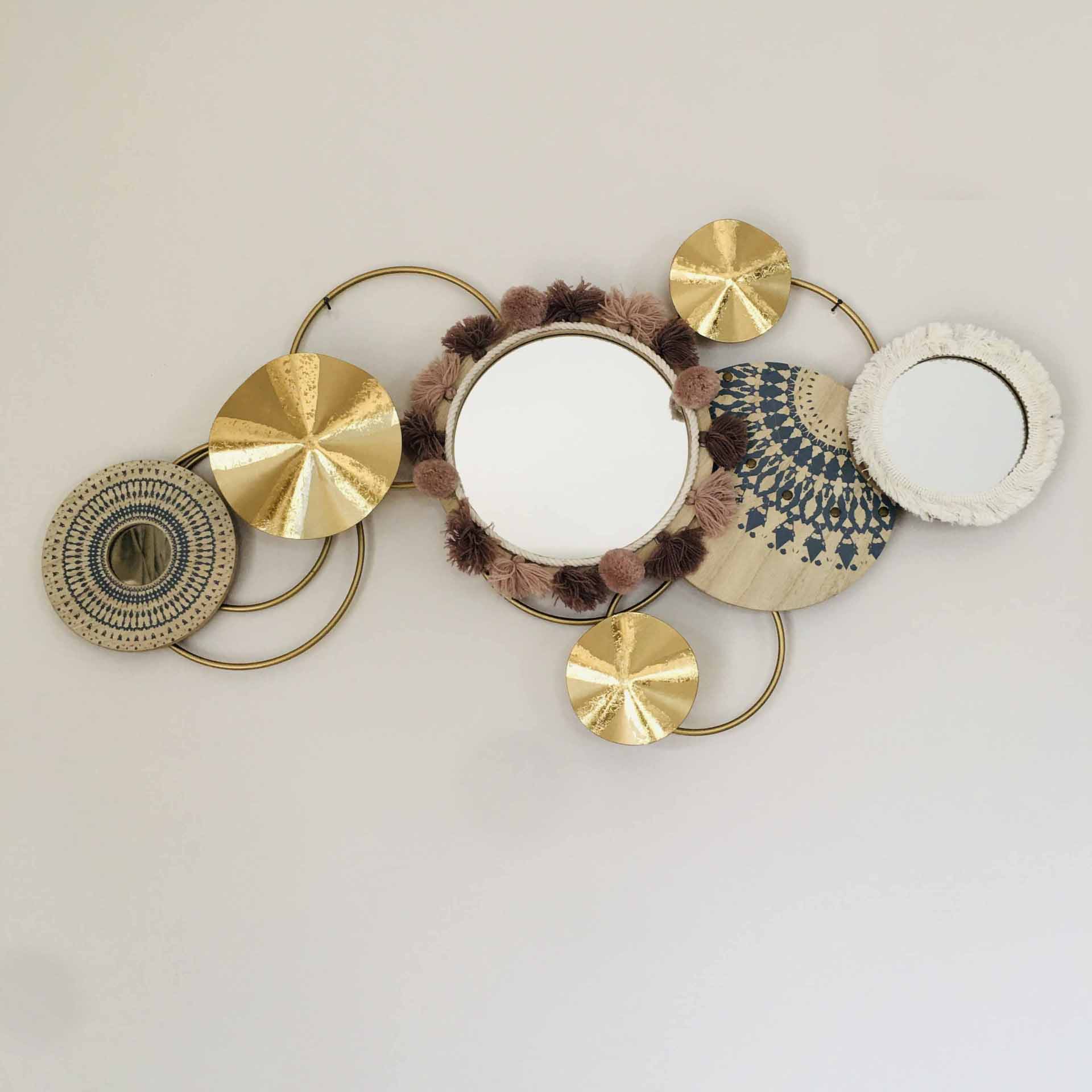 Decoração de parede com três espelhos redondos e elementos decorativos em metal dourado e fibras naturais