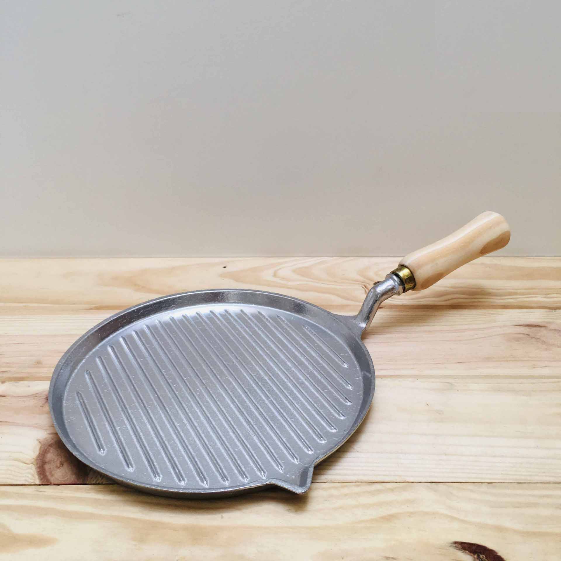 Frigideira de metal com ranhuras e alça de madeira sobre superfície de madeira