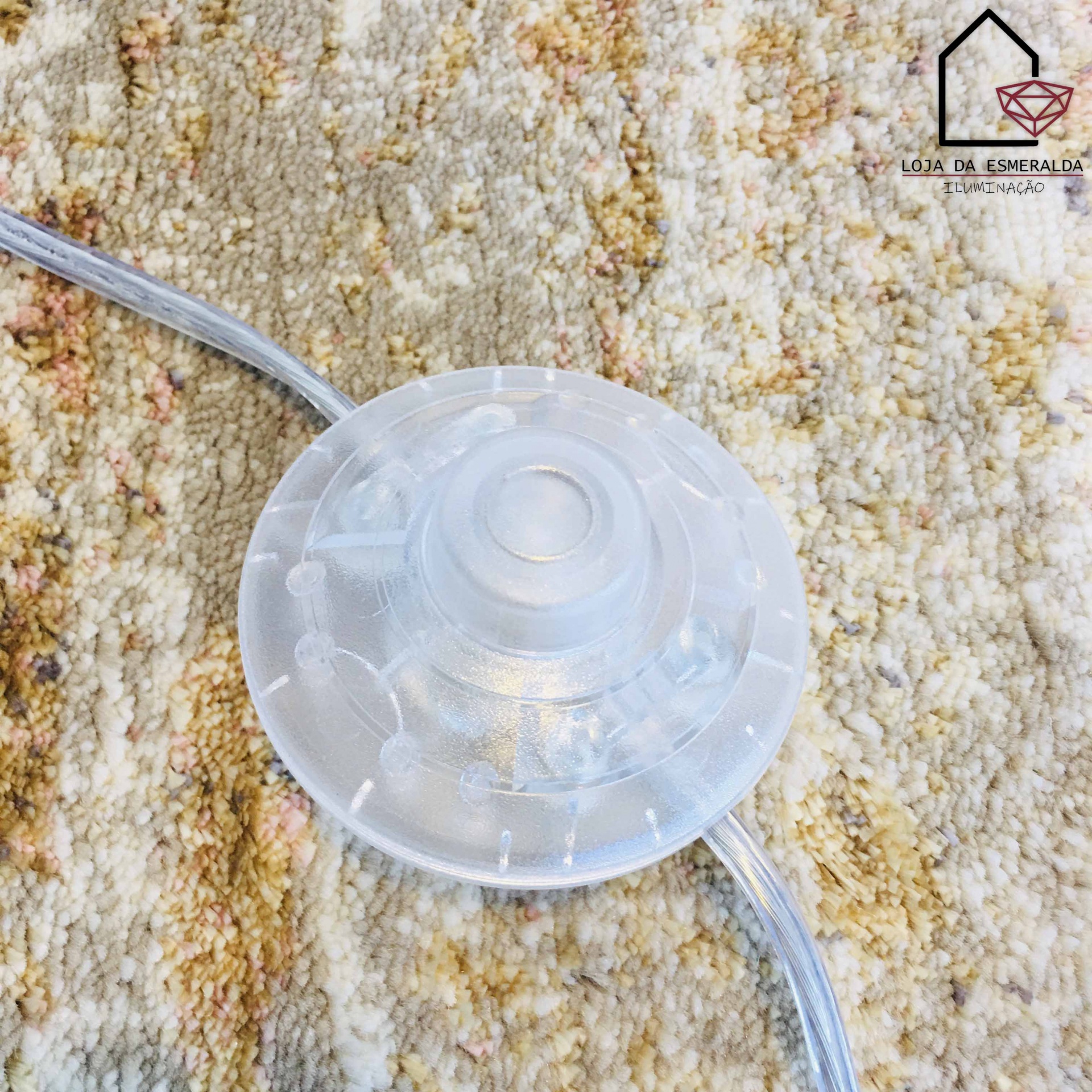 Interruptor redondo transparente com cabo sobre tapete bege e castanho