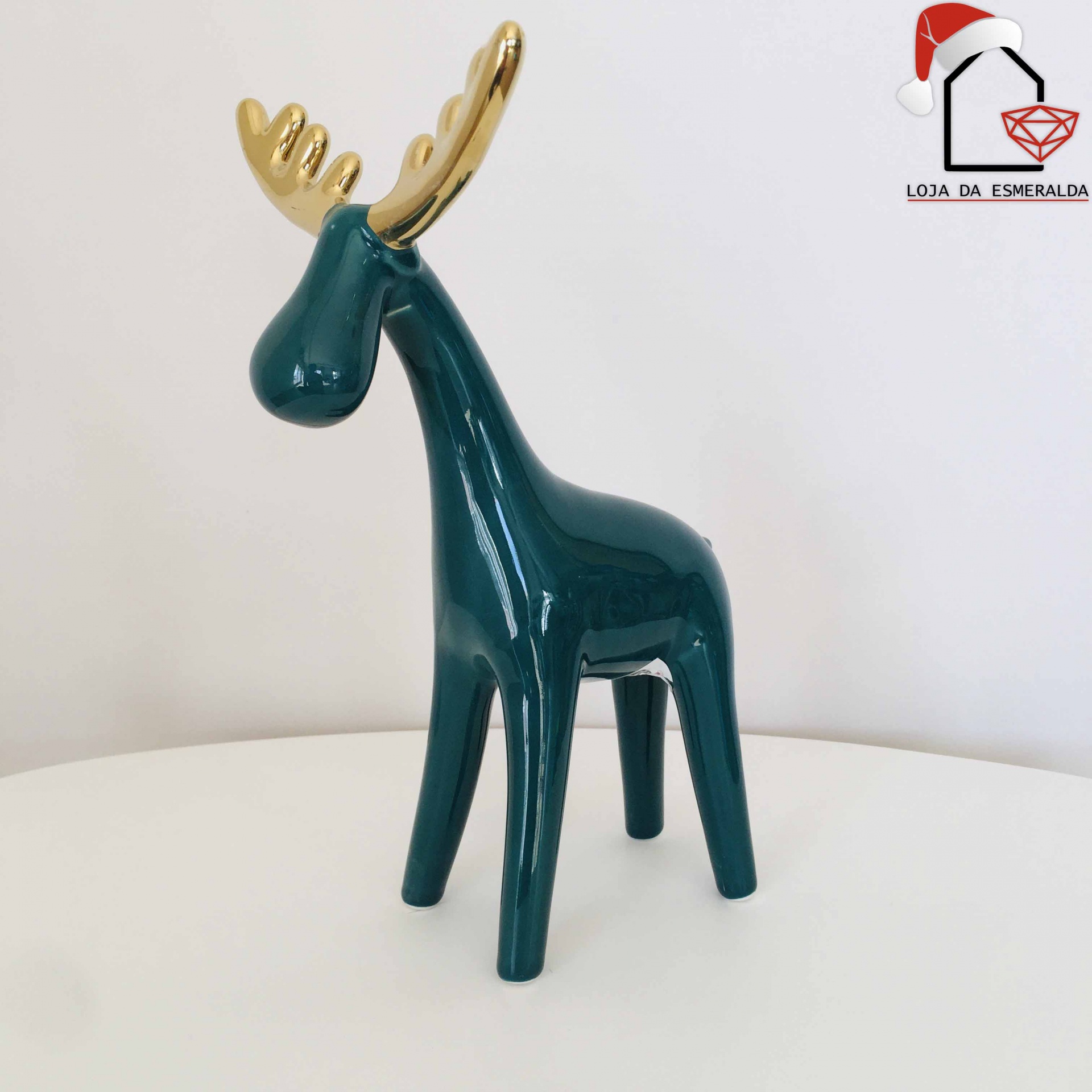 Escultura de rena em cerâmica verde com galhos dourados sobre superfície branca