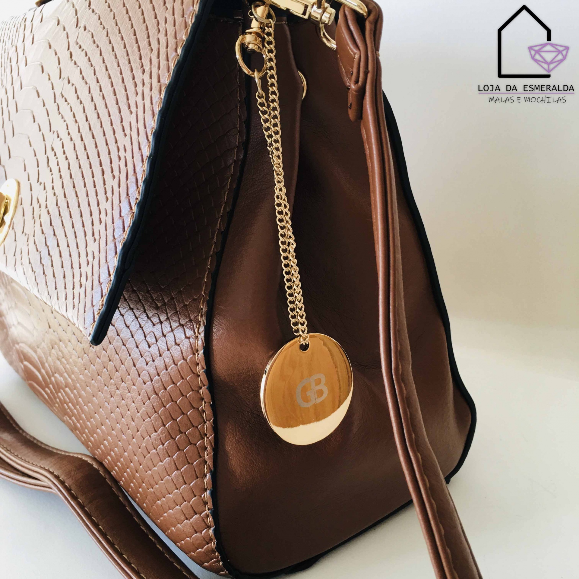 Bolsa de senhora castanha com textura de escamas e pendente redondo, sobre fundo branco com logótipo