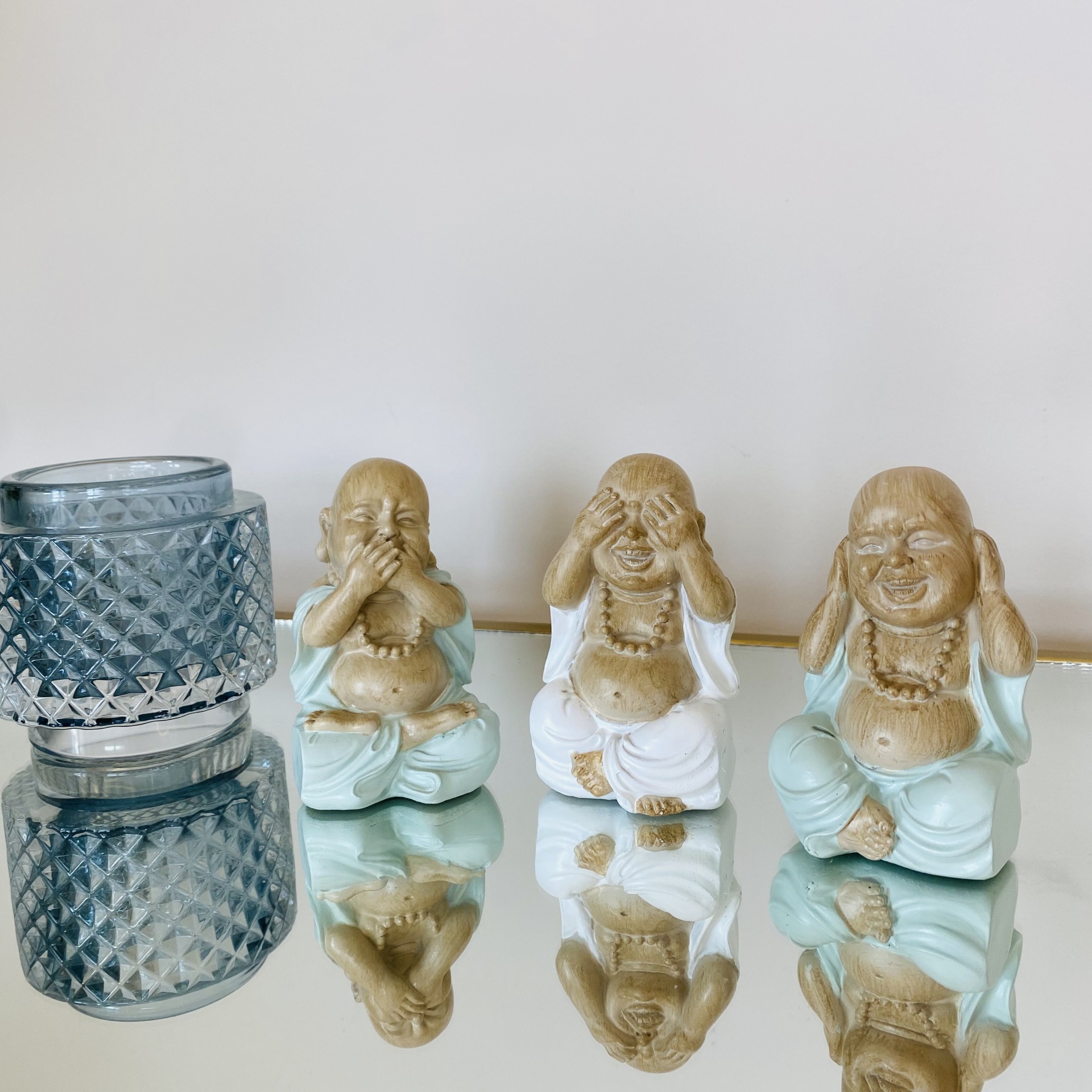 Três estatuetas de Buda em diferentes posturas com um copo de vidro ao lado