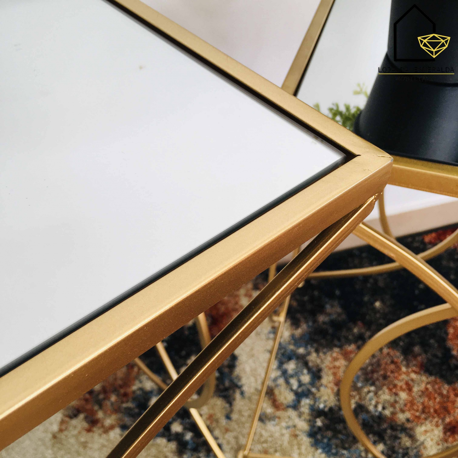 Mesa com tampo branco e moldura dourada metálica sobre tapete colorido