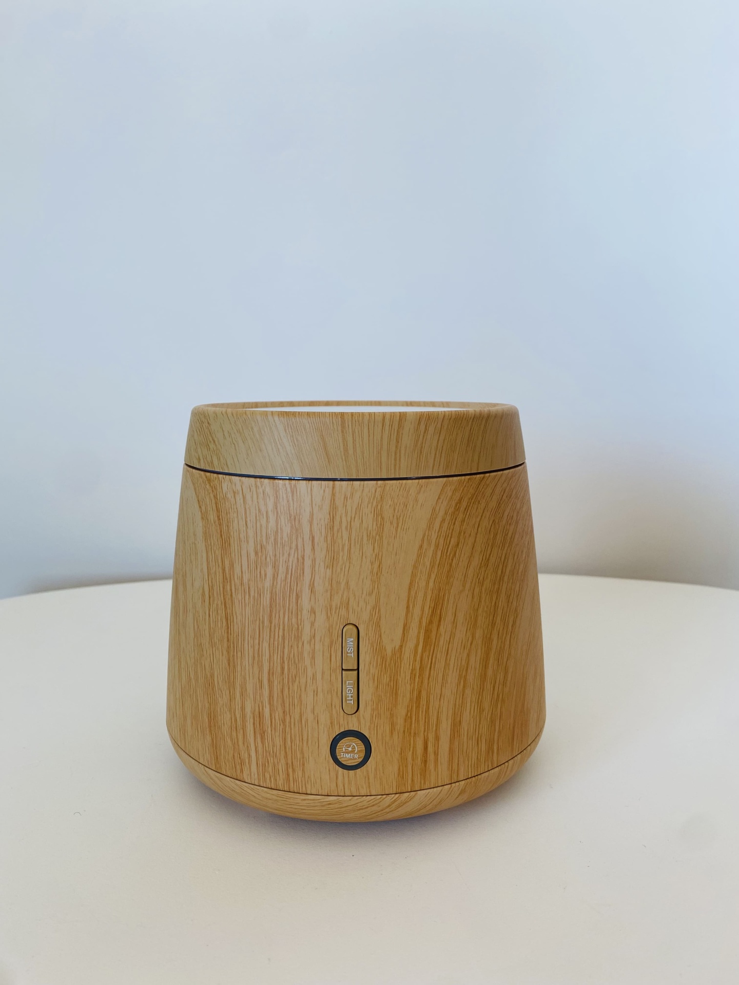 Difusor de ar em madeira clara com botões na frente, sobre superfície branca