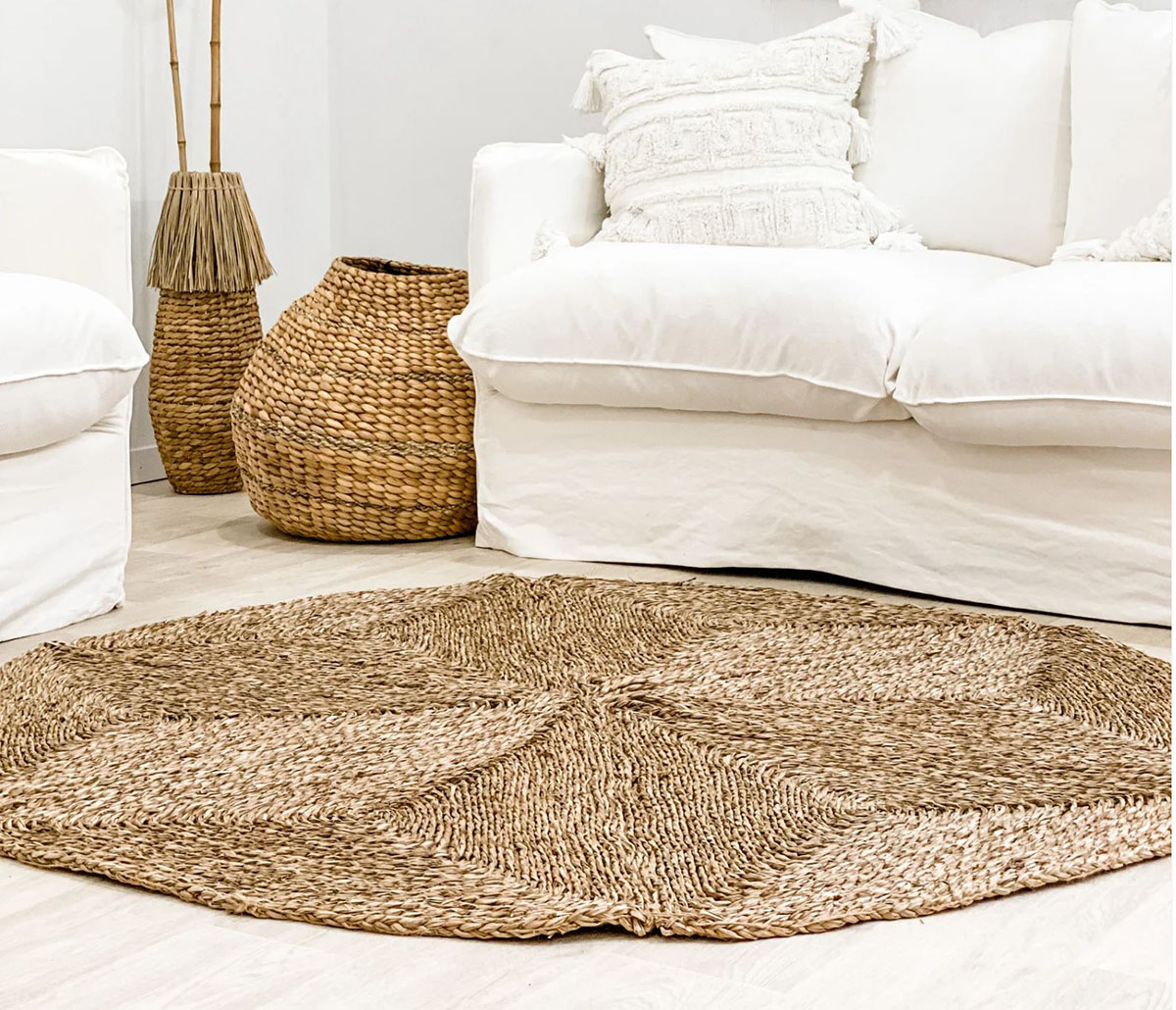 Tapete redondo trançado em fibras naturais castanhas com sofá branco e cestos decorativos
