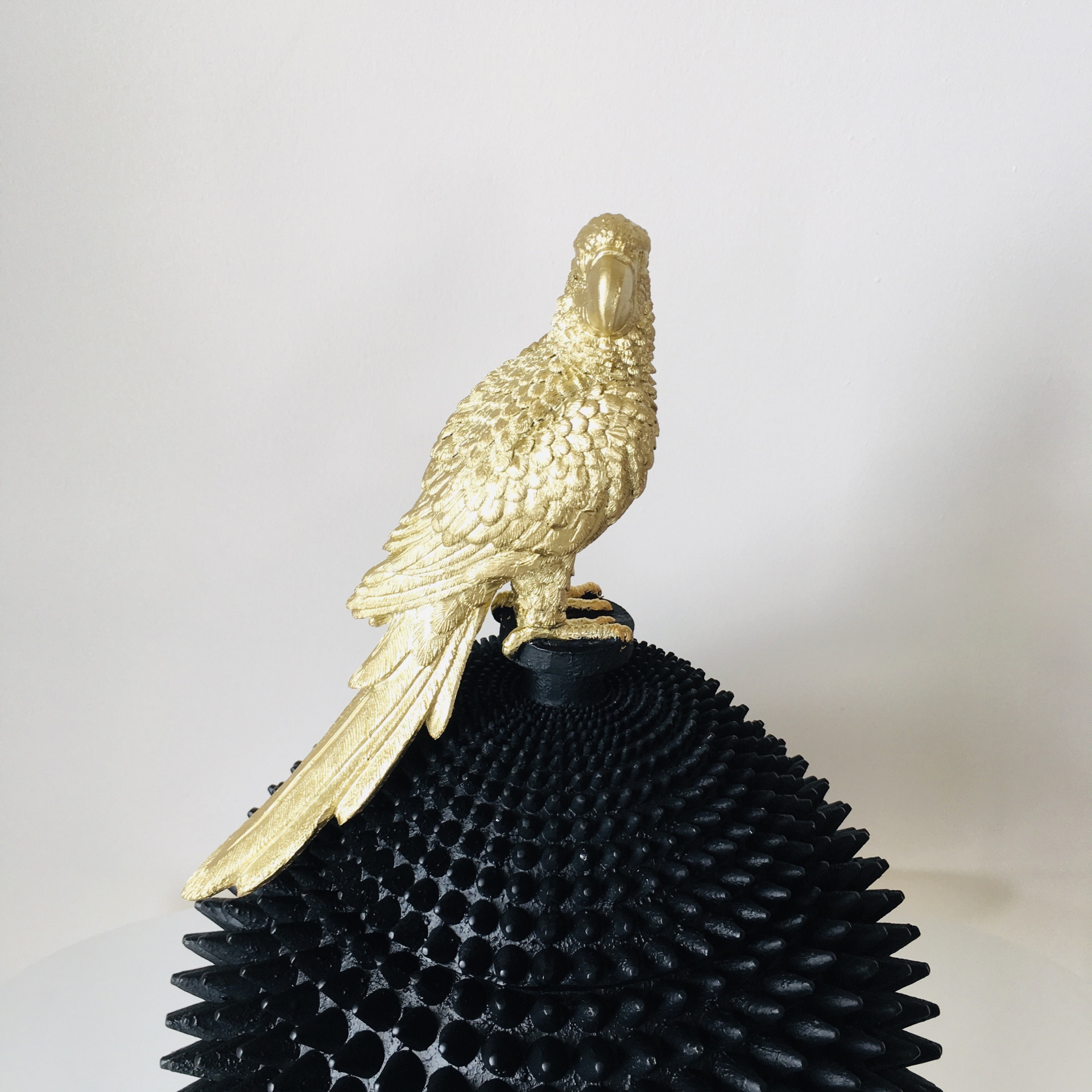 Estátua de pássaro dourado sobre base preta texturizada