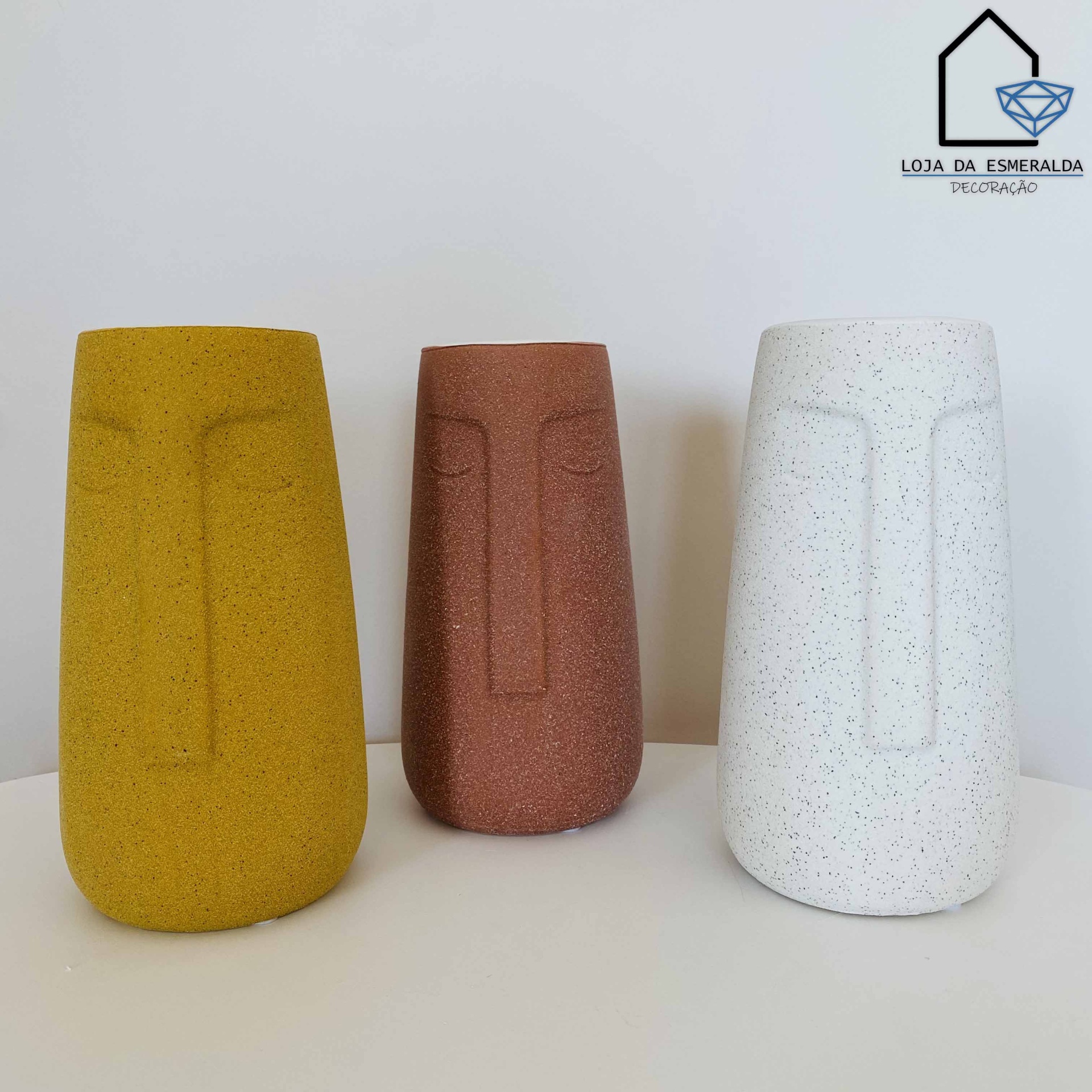 Três vasos decorativos em forma de rosto nas cores mostarda, terracota e branco com pintas