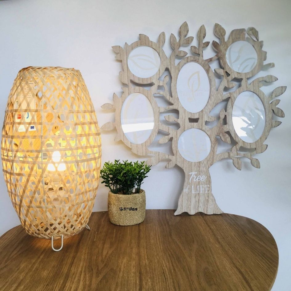 Abajur de luz quente com estrutura trançada de madeira, vaso tecido com planta verde, moldura árvore em madeira com mensagens, mesa de madeira.