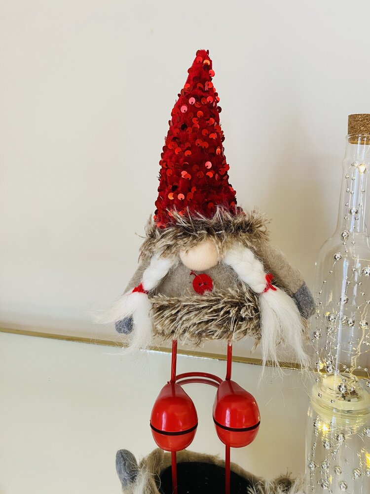 Boneco decorativo de Natal com chapéu vermelho e corpo peludo colocado sobre superfície branca ao lado de garrafa de vidro