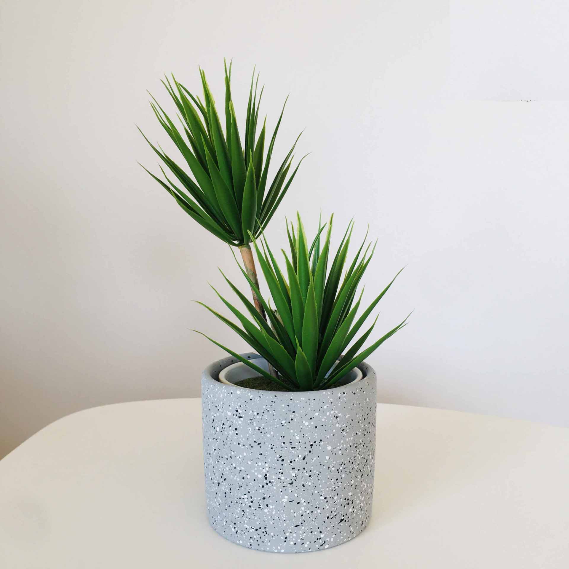 Planta artificial verde em vaso cinza pontilhado preto sobre superfície branca