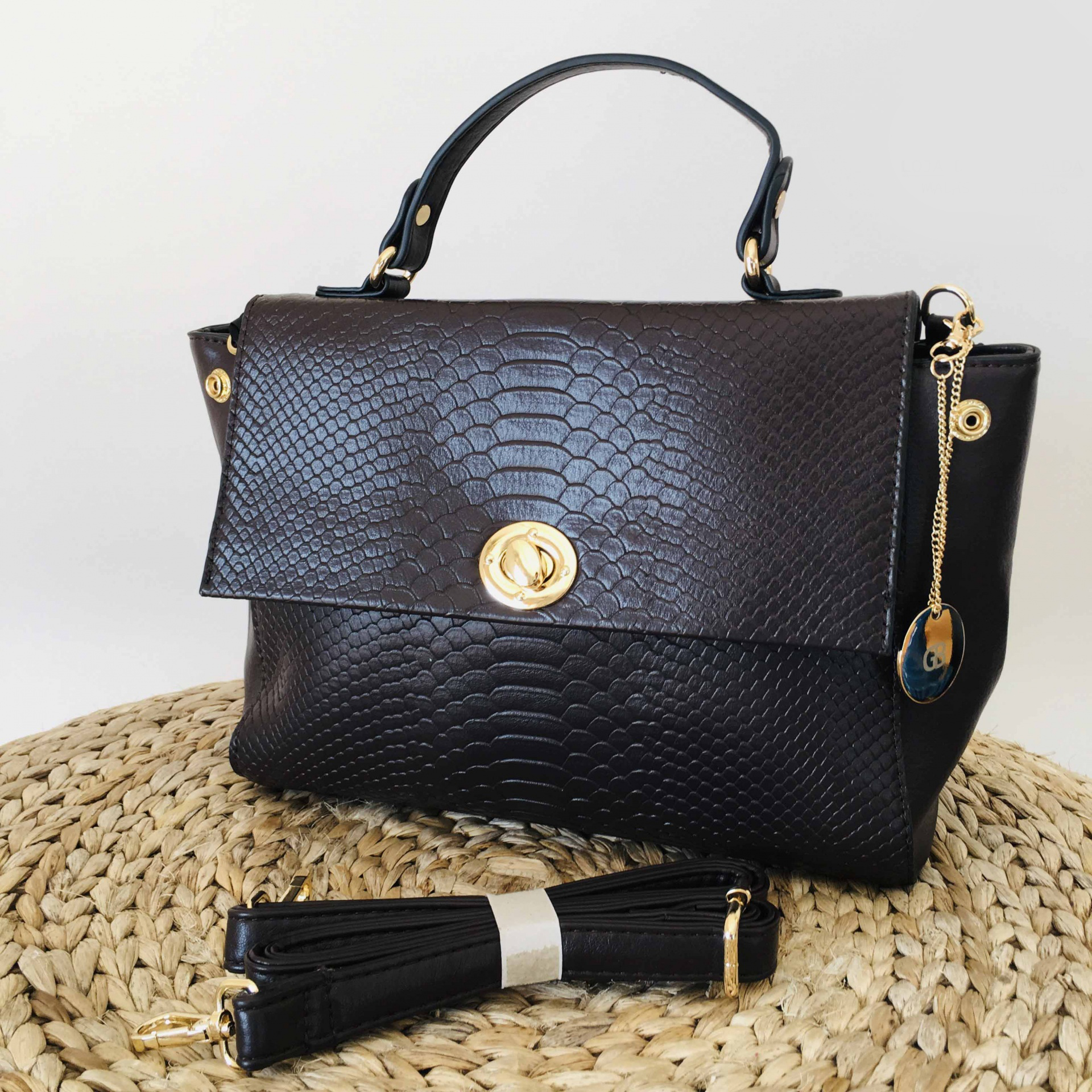Mala preta textura pele de crocodilo fecho dourado e corrente pendente em superfície de palha trançada