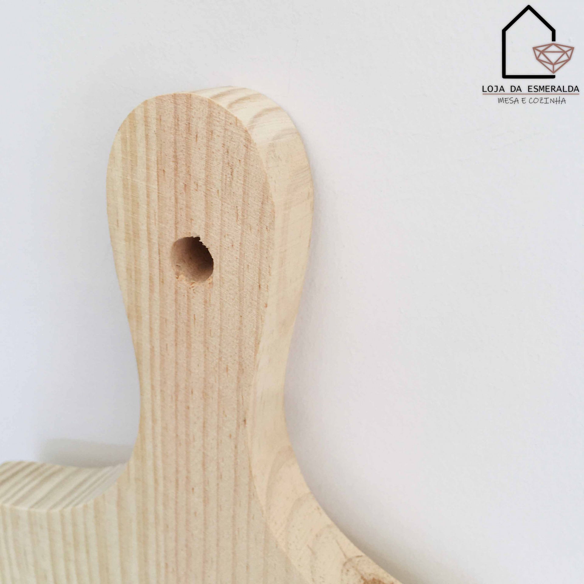 tábua de cortar madeira clara com furo redondo junto à parede branca e logotipo Loja da Esmeralda