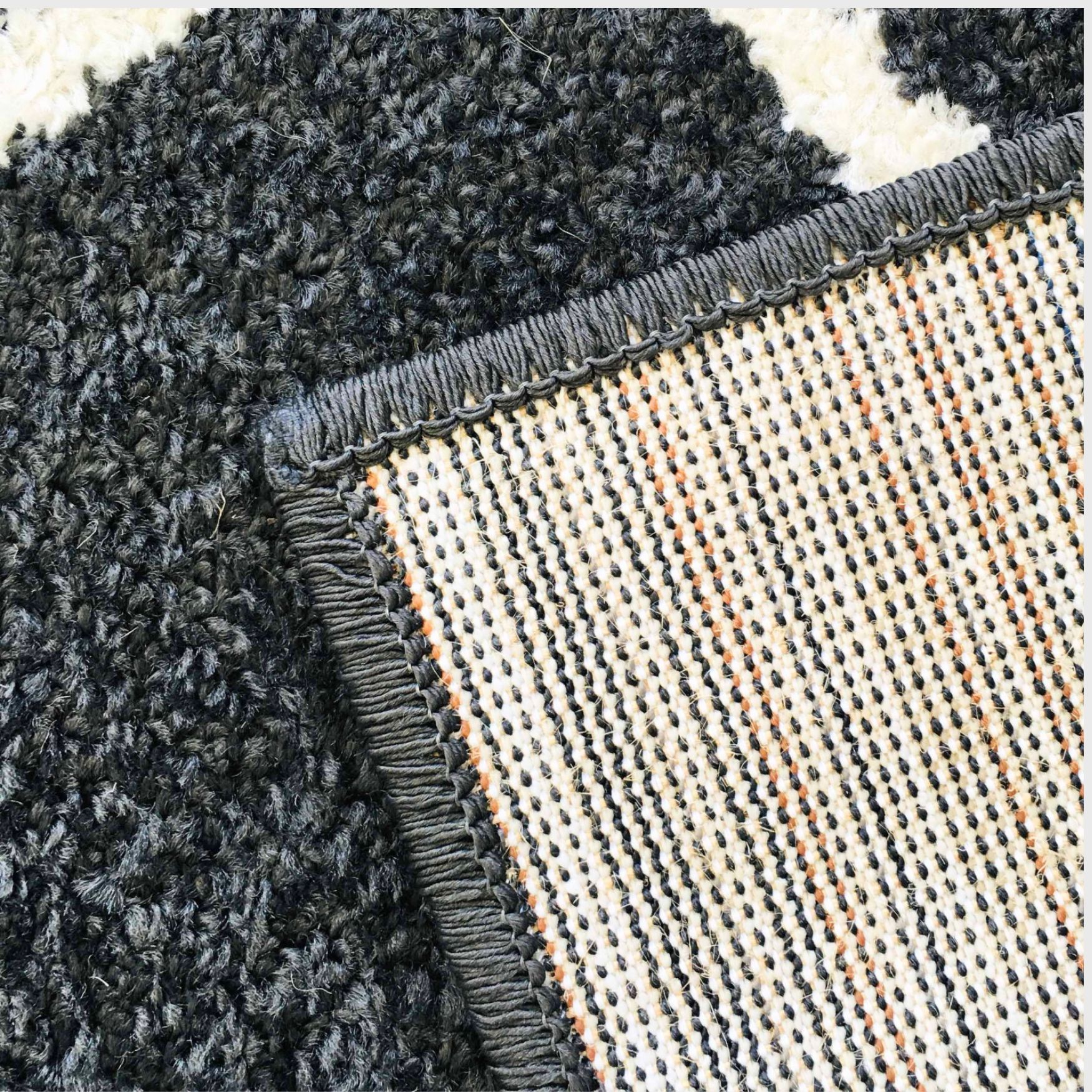 Tapete preto e branco com textura felpuda e parte inferior com costura cinza e padrão tecido