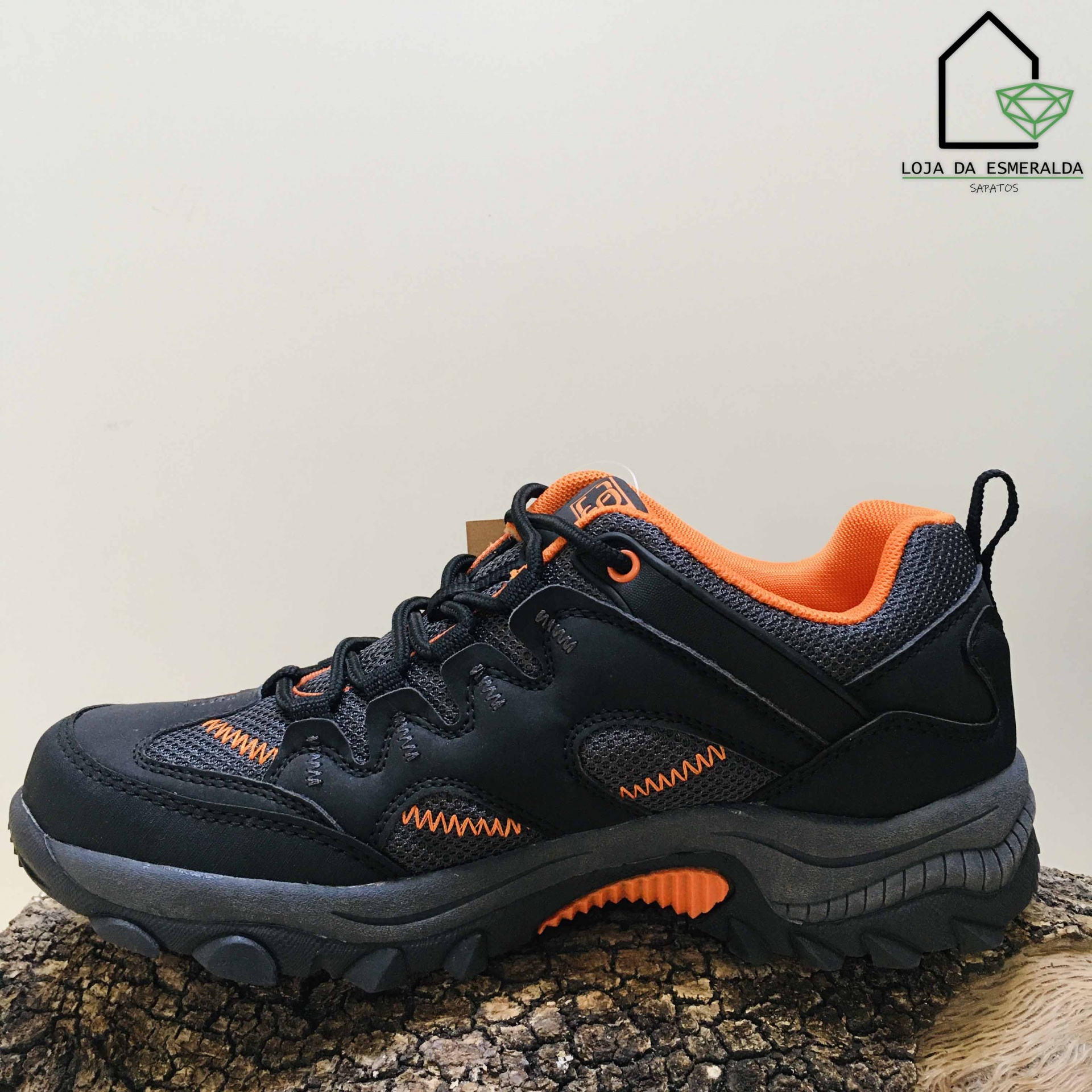 Tênis desportivo preto e laranja sobre tronco com fundo branco e logo da loja