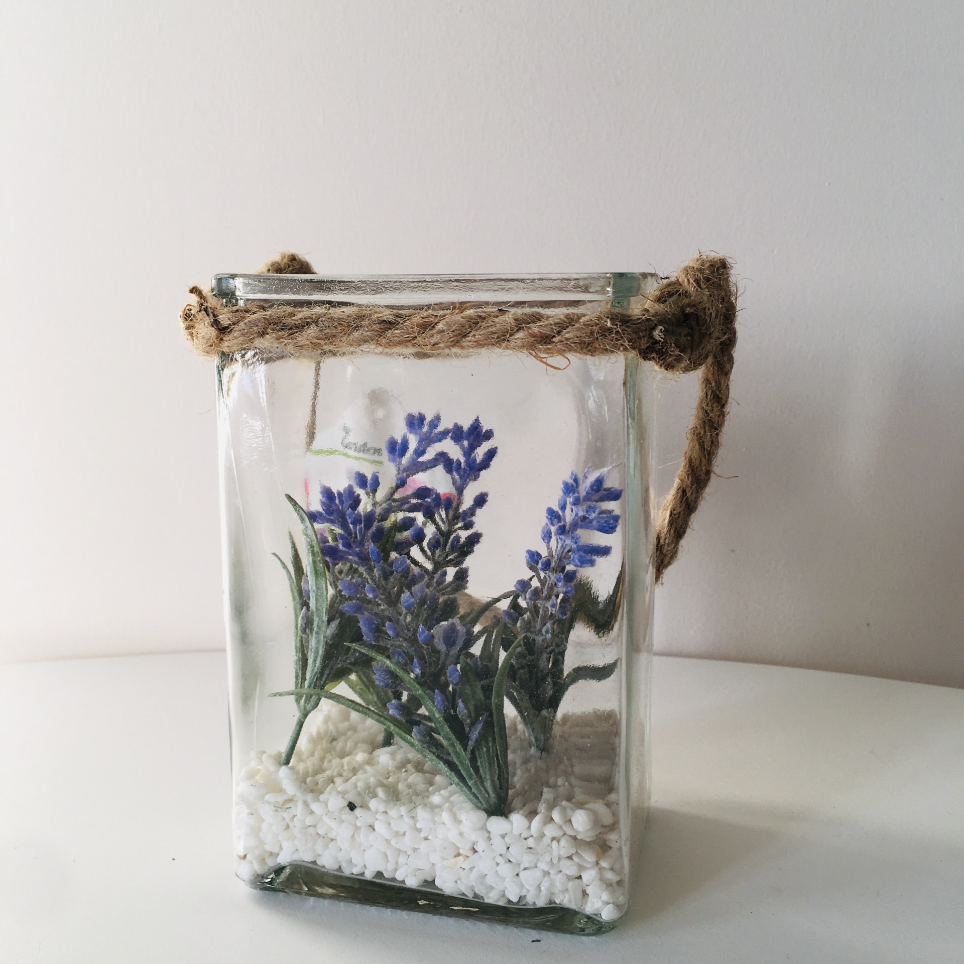 Frasco de vidro com flores artificiais roxas e pedrinhas brancas, alça de corda rústica
