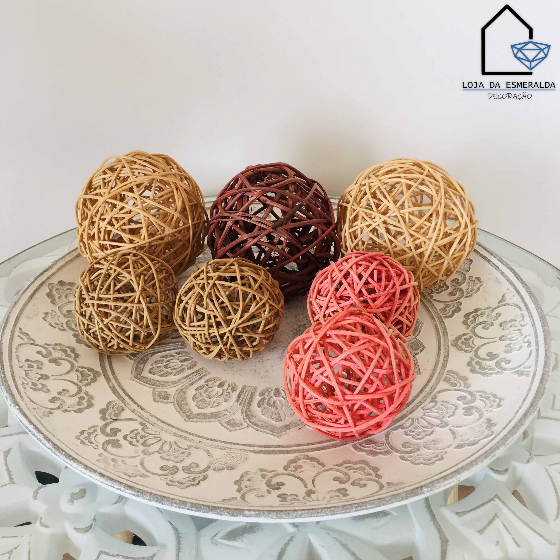 Bolas decorativas de rattan em várias cores num prato decorativo com padrão floral.