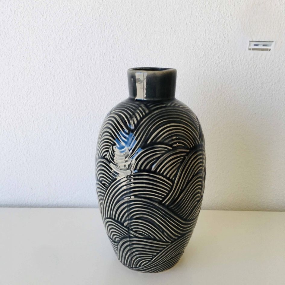 Vaso decorativo em cerâmica preta com padrões brancos ondulados colocado numa superfície branca
