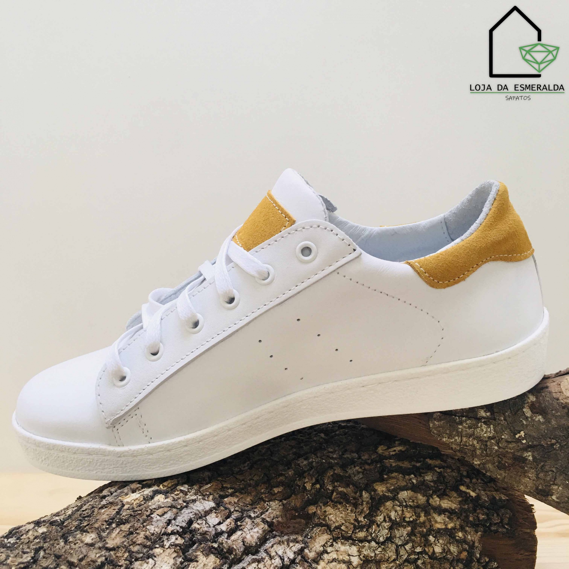Ténis branco com detalhes amarelos sobre tronco de árvore