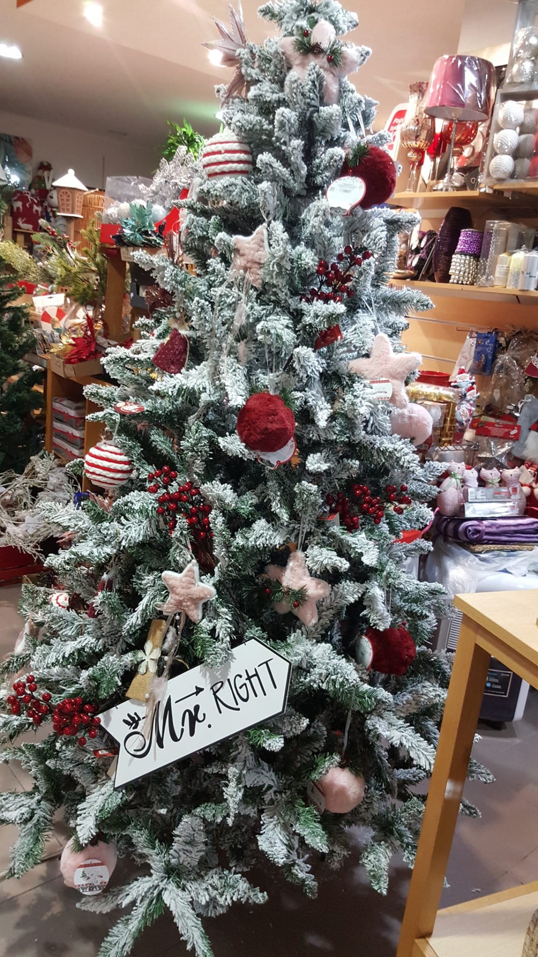 Árvore de Natal coberta de neve e enfeites vermelhos e rosa, placa com 