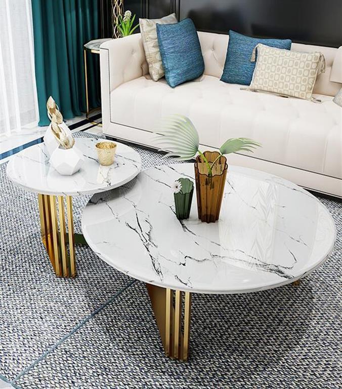 Conjunto de mesas de centro em mármore branco com bases douradas, sofá branco com almofadas coloridas ao fundo