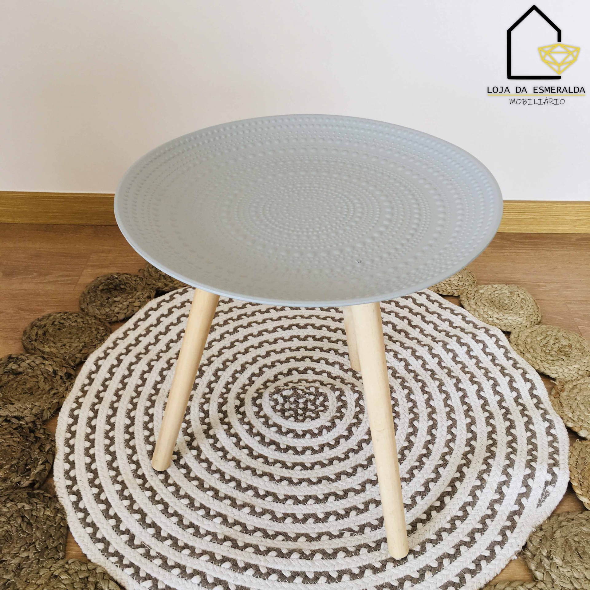 Mesa redonda cinzenta com patas de madeira clara sobre tapete redondo com padrões em castanho, bege e branco