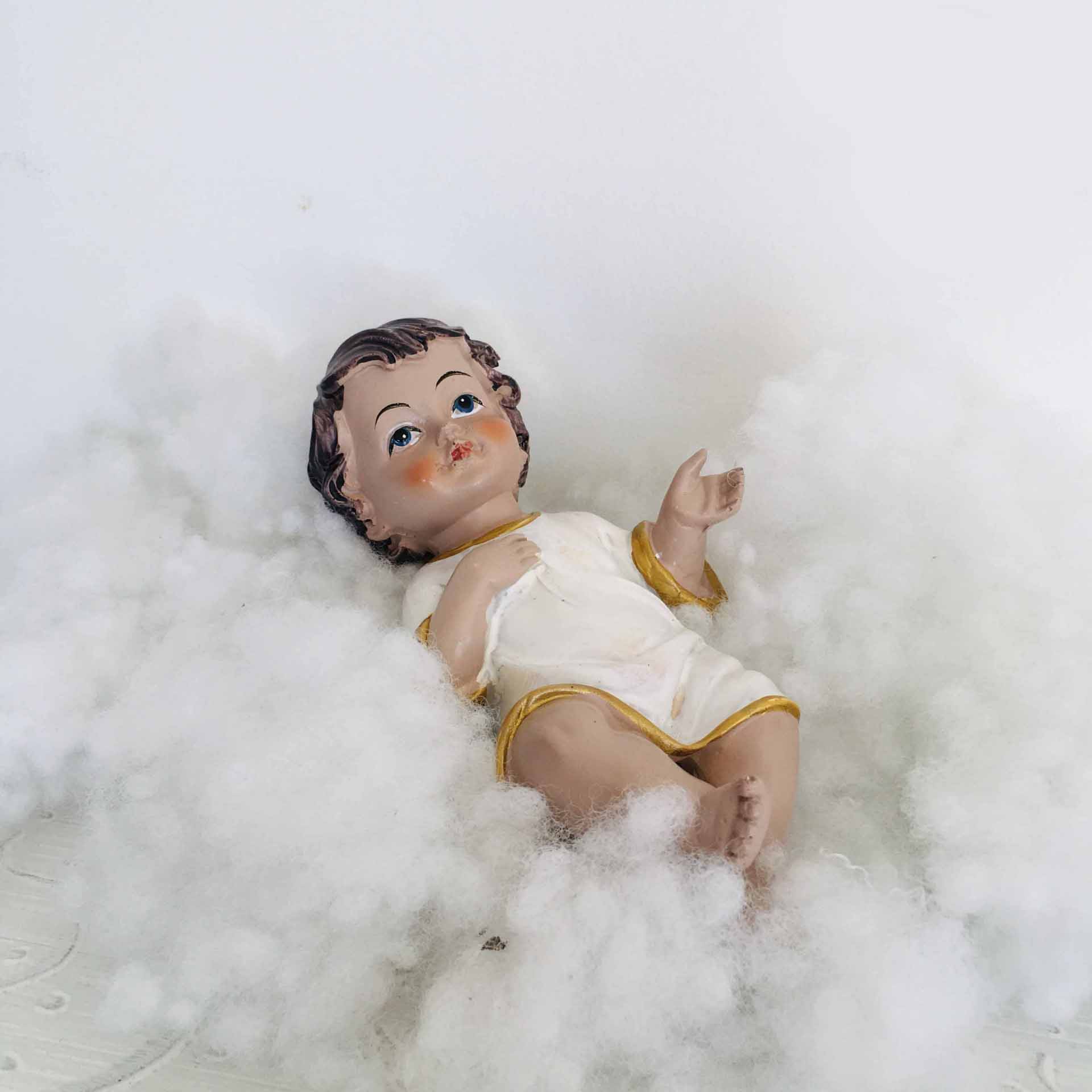 Figura de Jesus menino em túnica branca com bordas douradas sobre algodão branco