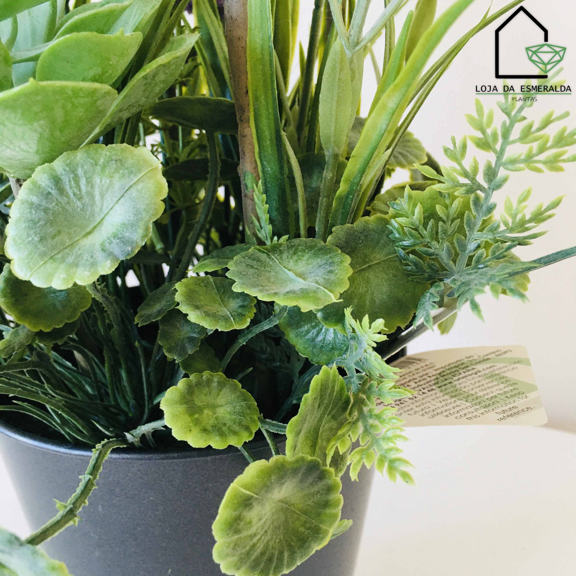 Arranjo de plantas artificiais em vaso cinza com folhas verdes variadas