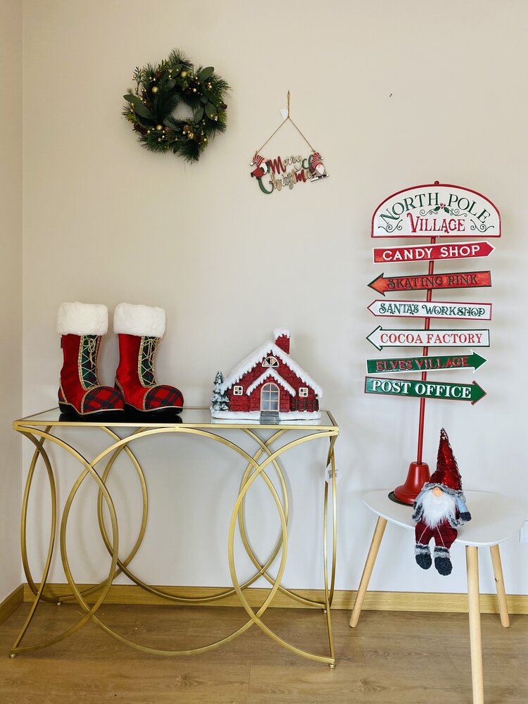 Decoração natalícia com botas vermelhas, casa de gengibre, gnomo, placa de setas com textos de Natal, guirlanda e enfeite na parede