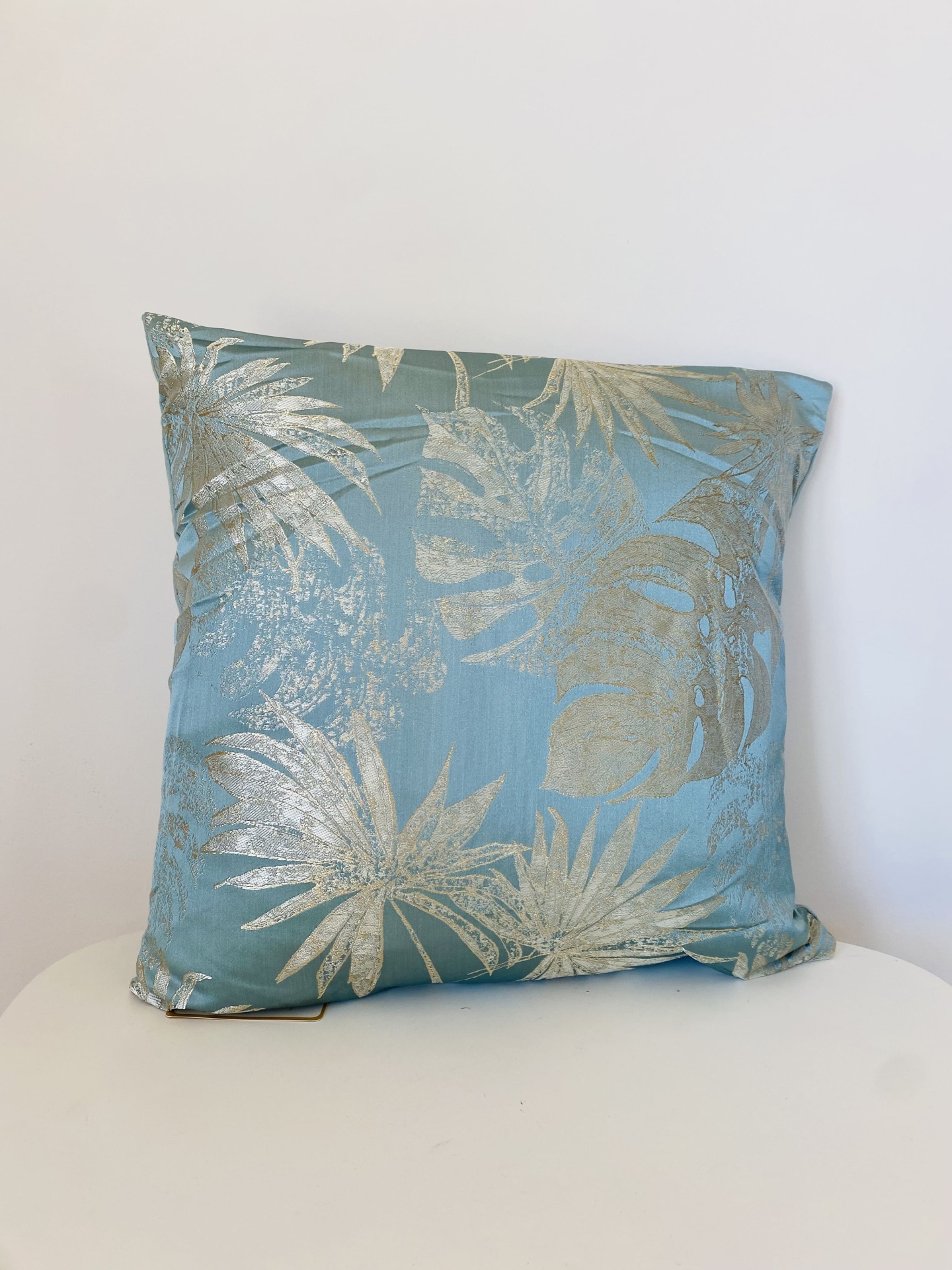 Almofada azul claro com padrão dourado de folhas tropicais