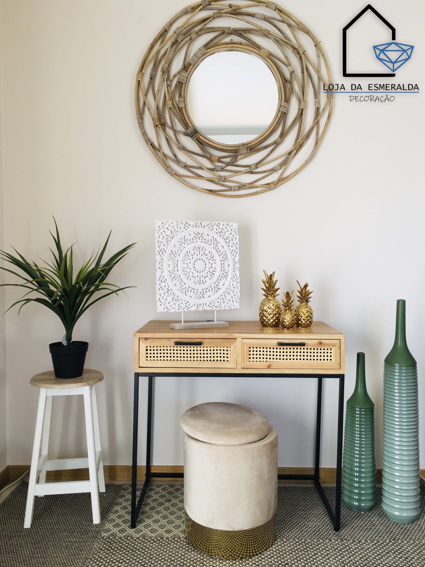 Mesa com gavetas de rattan, objetos decorativos dourados, escultura branca, espelho redondo de madeira, banco estofado, vaso verde e planta em vaso preto sobre banco branco