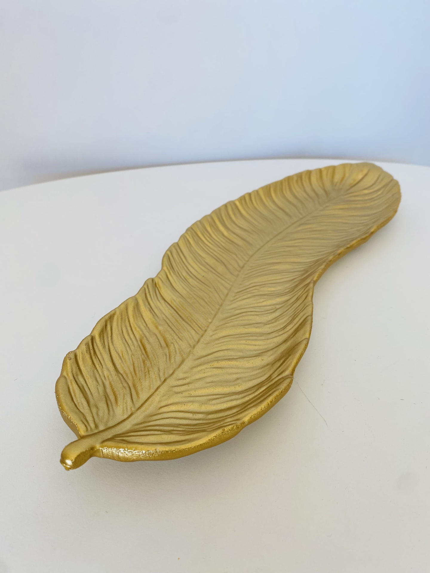 Prato decorativo dourado em forma de folha sobre superfície branca