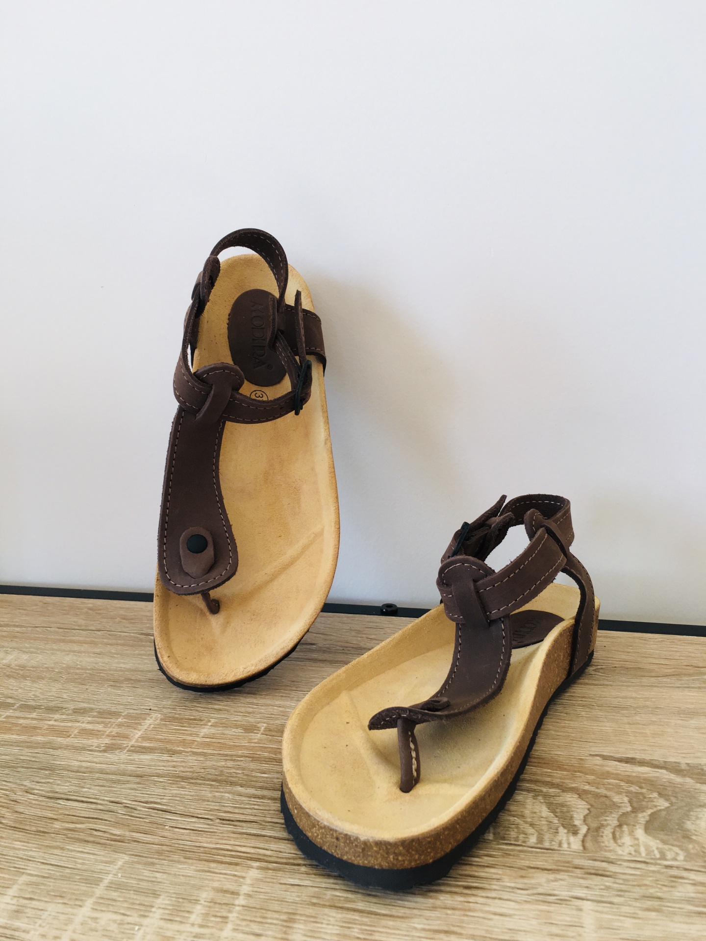 Sandálias de dedo castanho com palmilha bege sobre madeira
