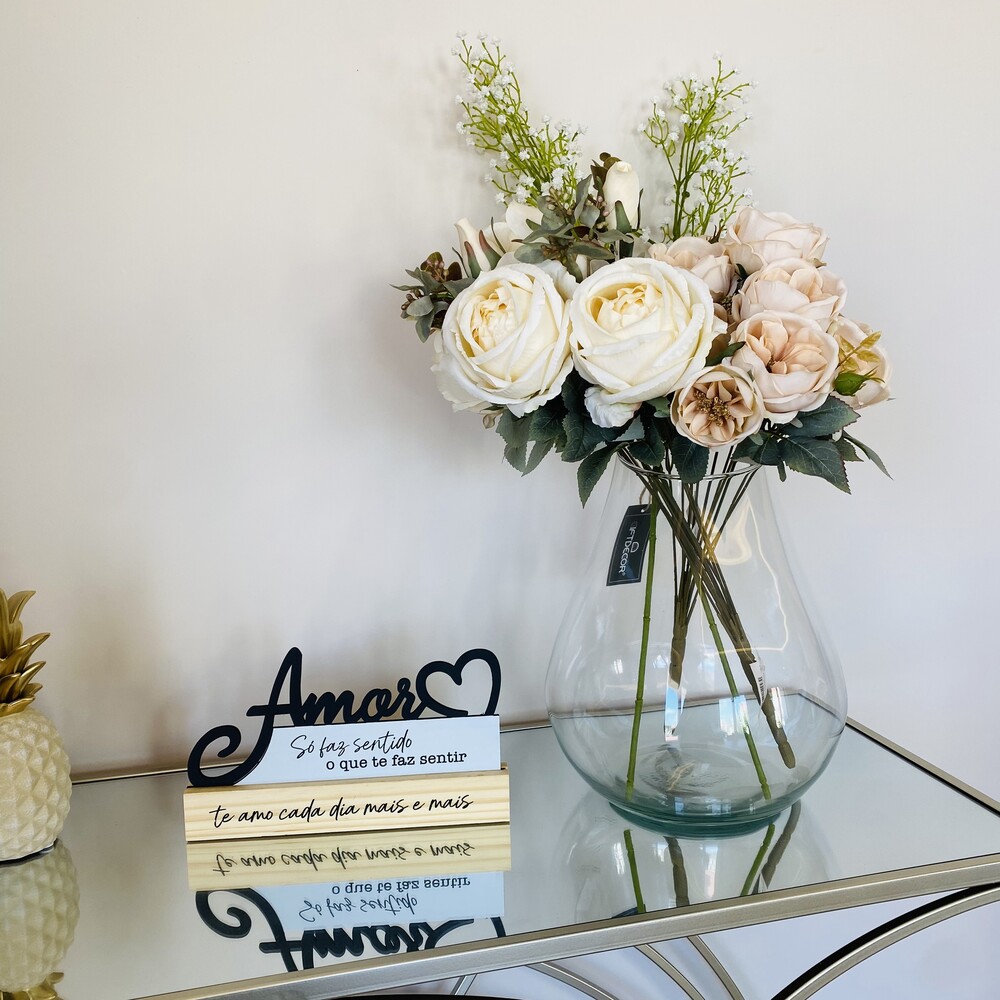 Arranjo de flores artificiais num vaso de vidro junto a placa decorativa com palavra Amor